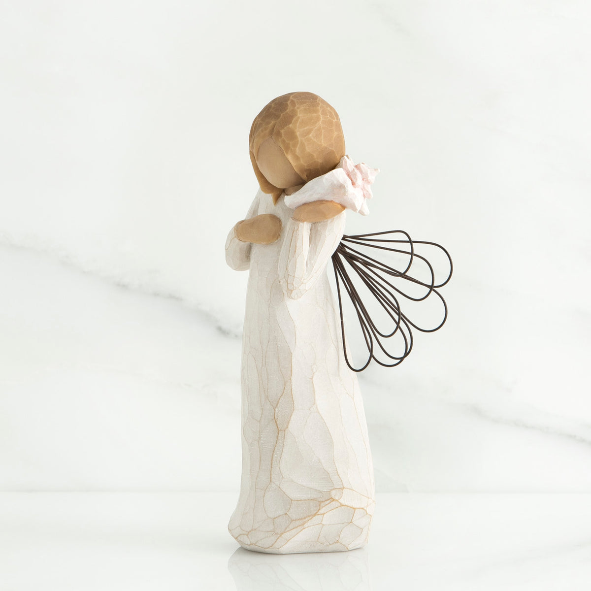Side view of blonde angel figurine holding white seashell to her ear
