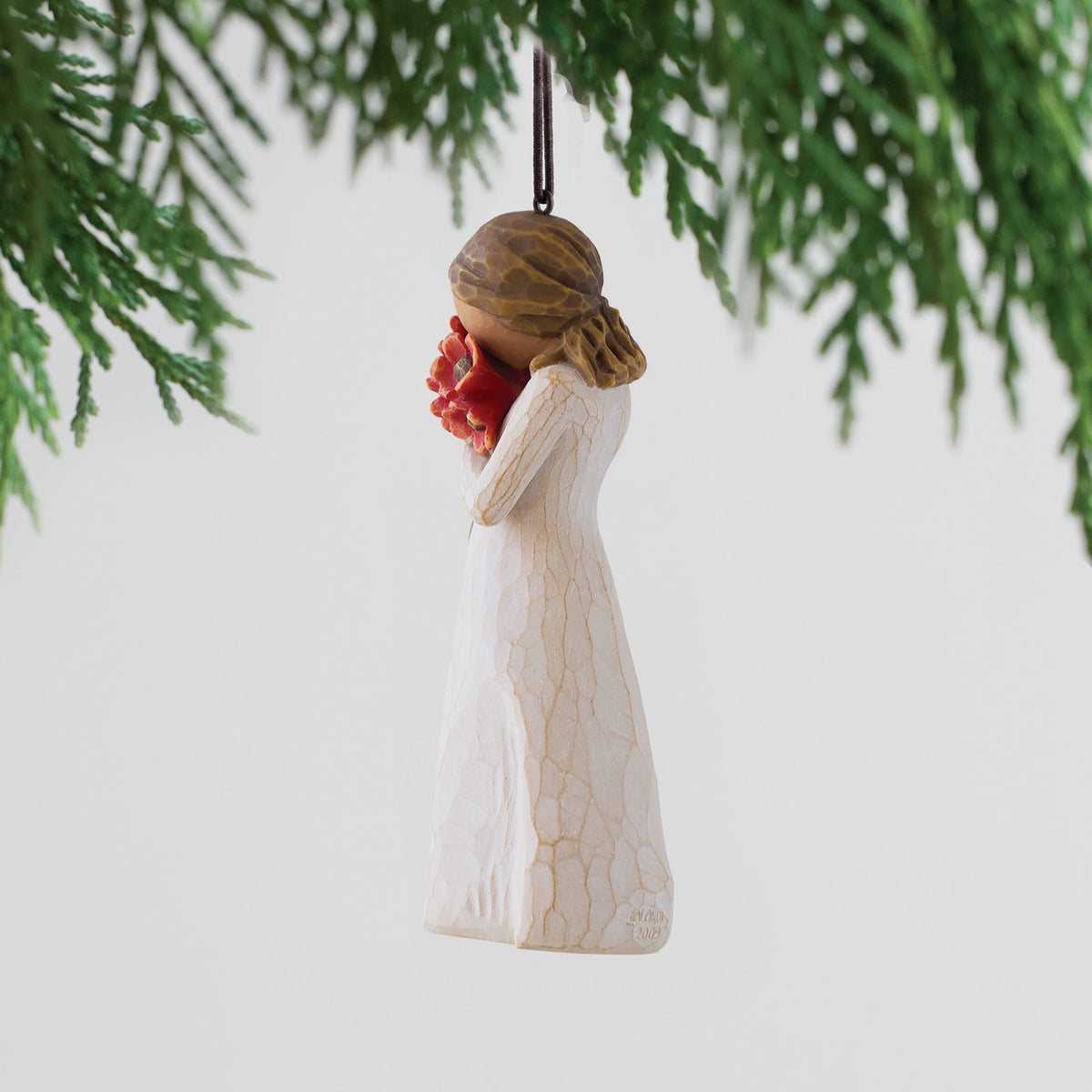 Figure in cream dress holding large bouquet of red-orange poppies up to face, ornament hook attached to head