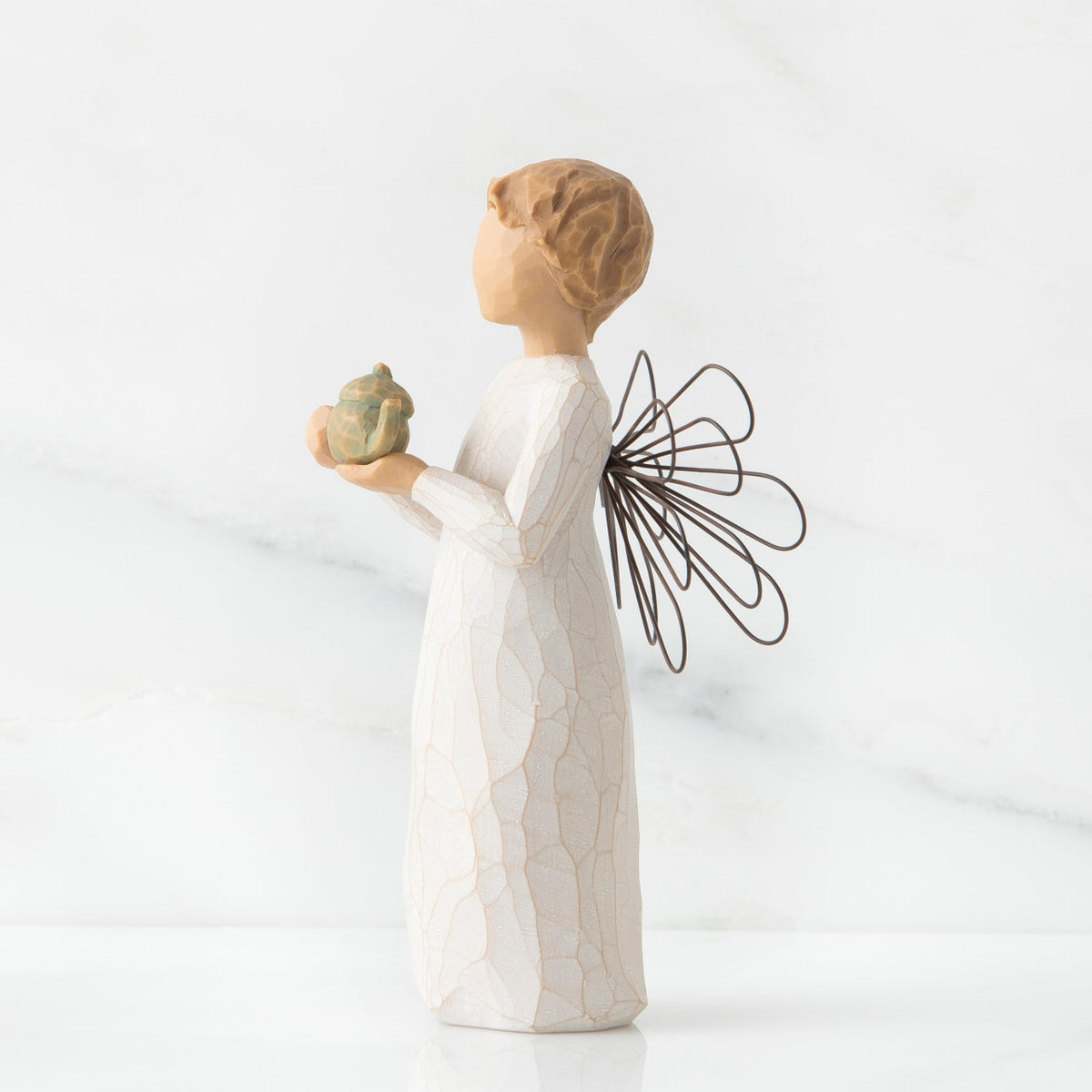 Angel figurine in white with black wings facing the side holding golden teapot figurine