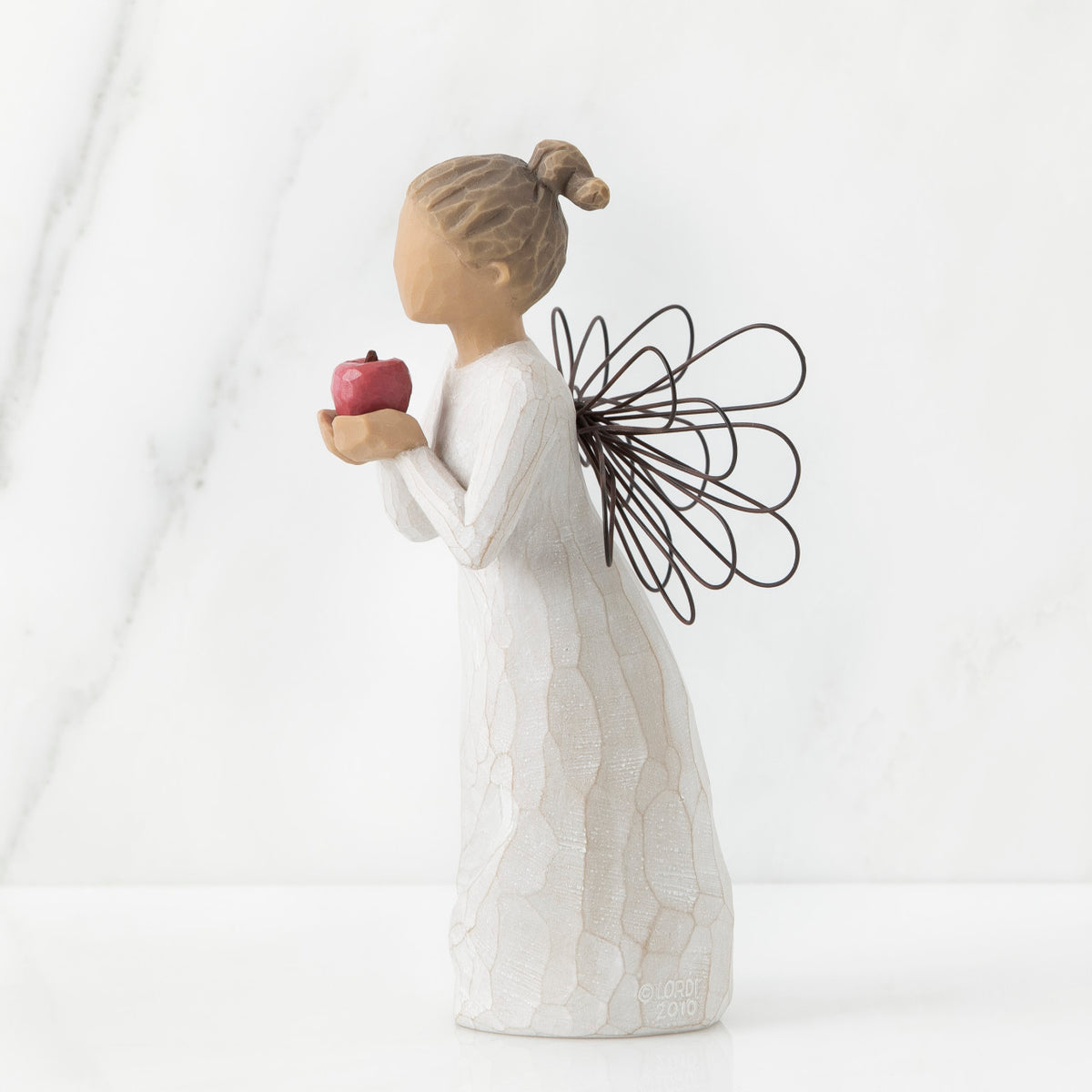 Right side view of angel with brown hair in high pony tail leaning forward and holding a red apple up to her face with both hands