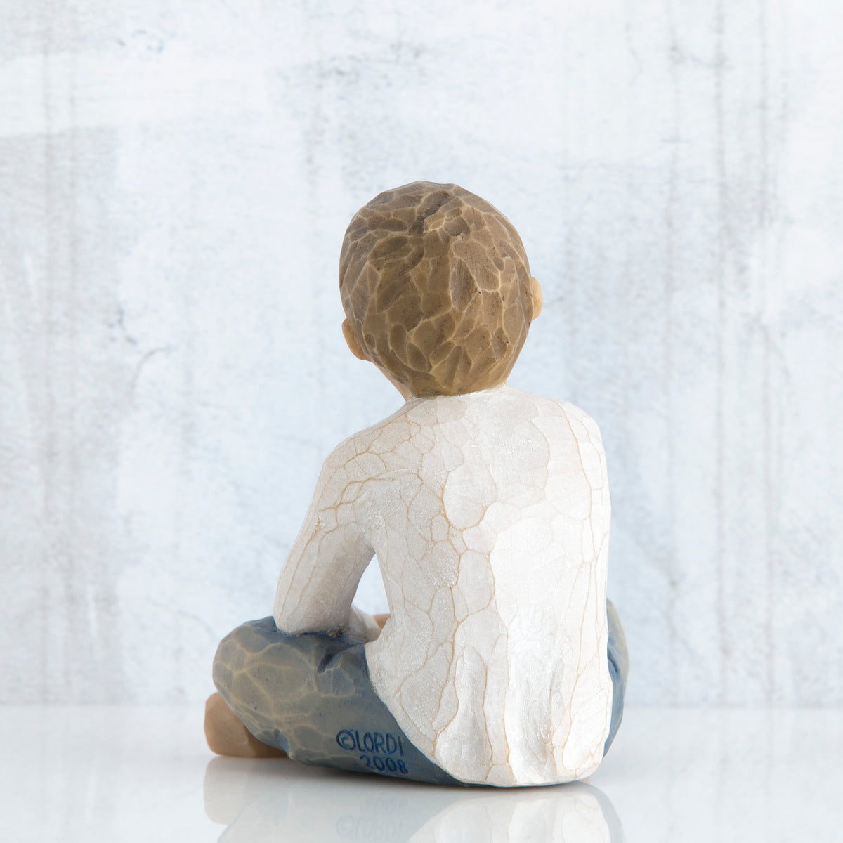 Back view of young brunette boy in white shirt and blue jeans sitting down
