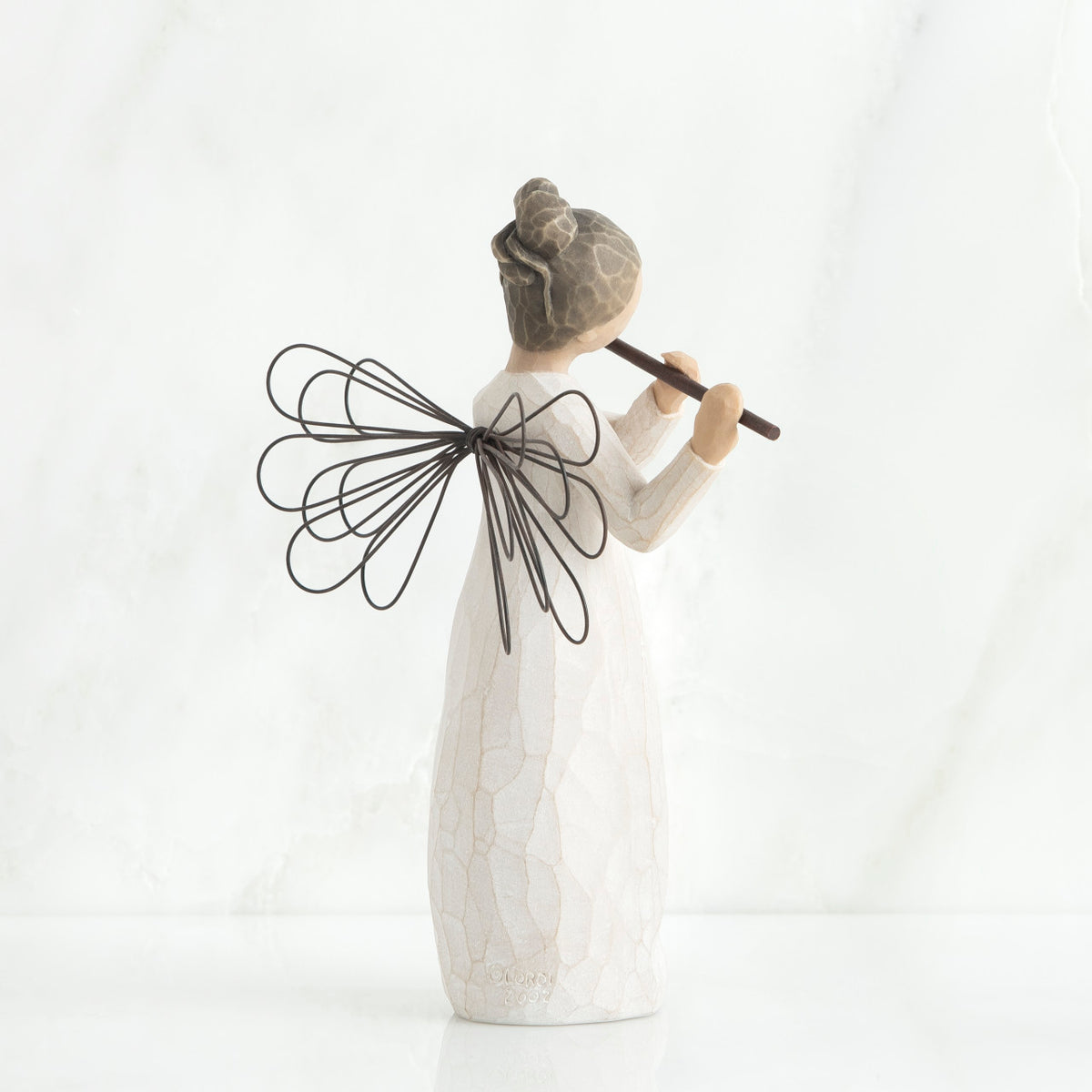 Back view of brunette angel figurine in white dress, black wings, and playing the flute