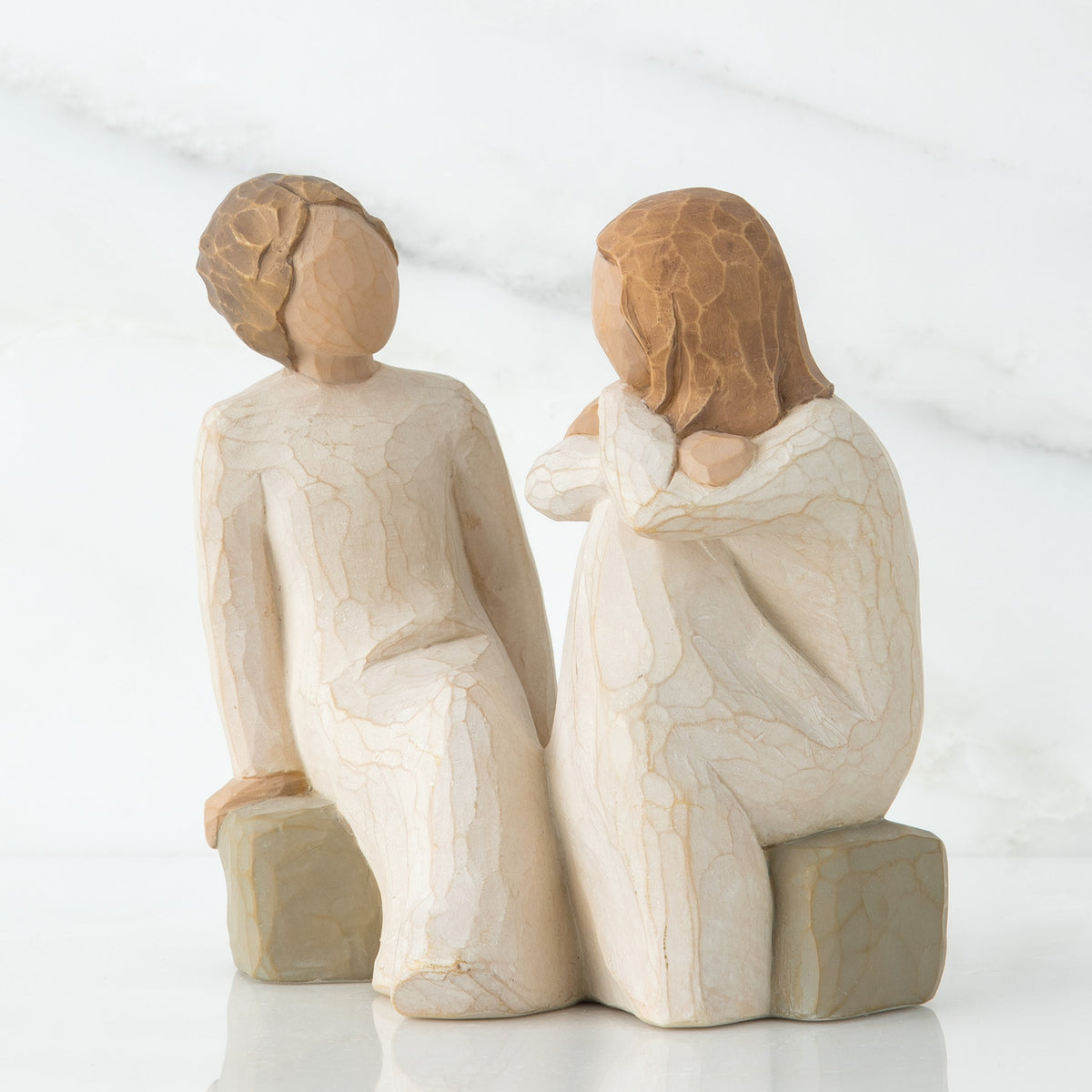 Two red haired girl figurines in white dresses sitting down on rocks