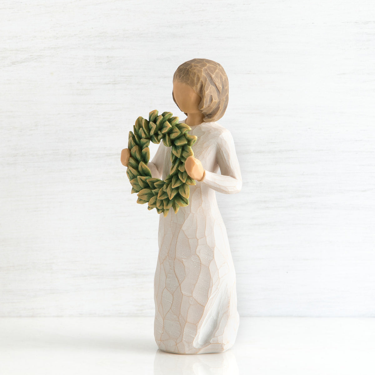 Right side view of young girl with bangs and short brown hair holding up a green, leafy wreath