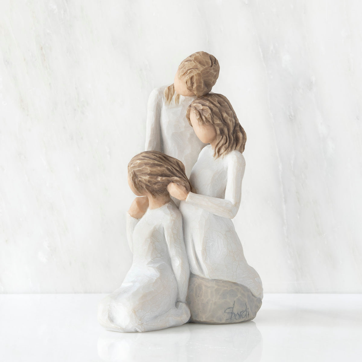 Left-facing view, figurine of three females in cream dresses: one standing with arm around kneeling female, and holding hand of seated female