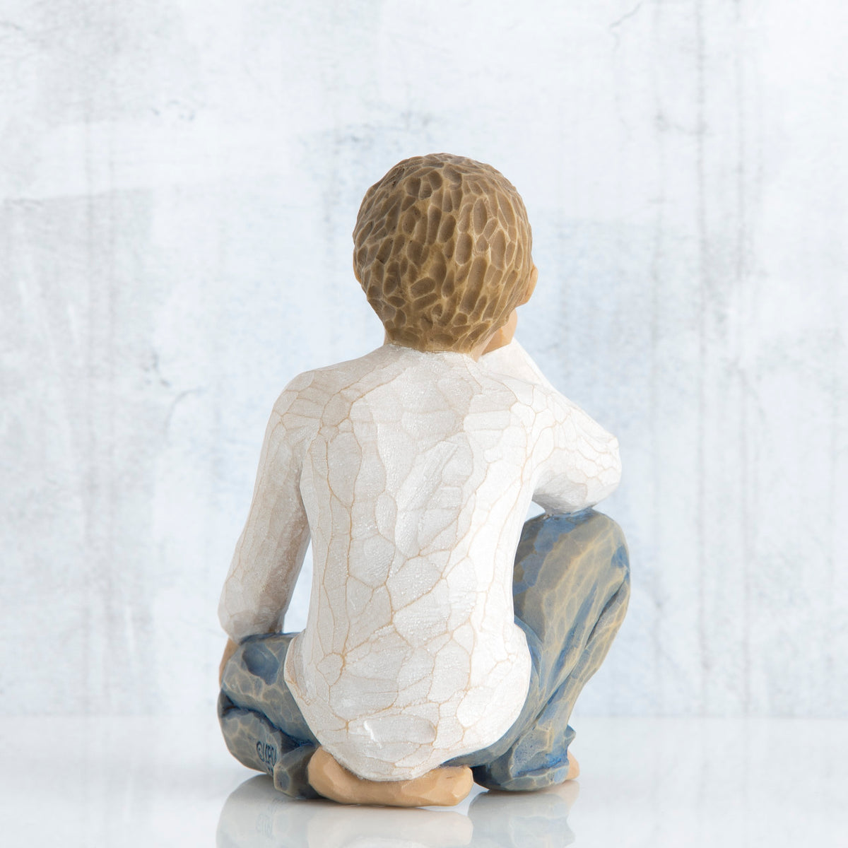 Back view of brunette boy figurine in white shirt and blue jeans sitting down