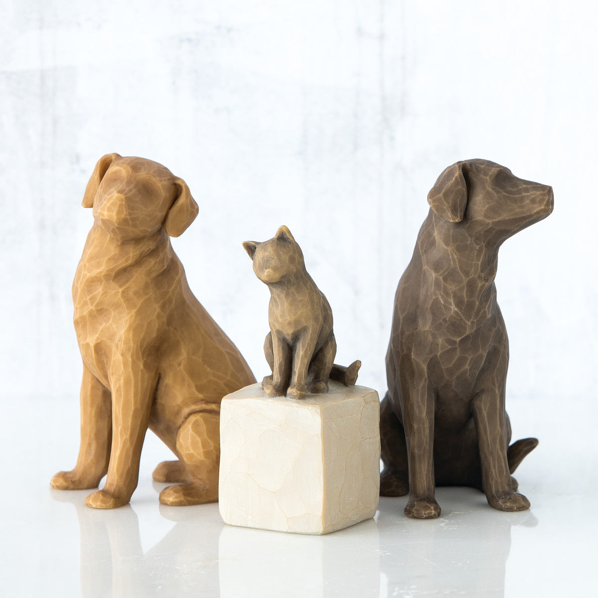 Set of two golden and brown dog figurines sitting in between one bronze cat figurine on a rock