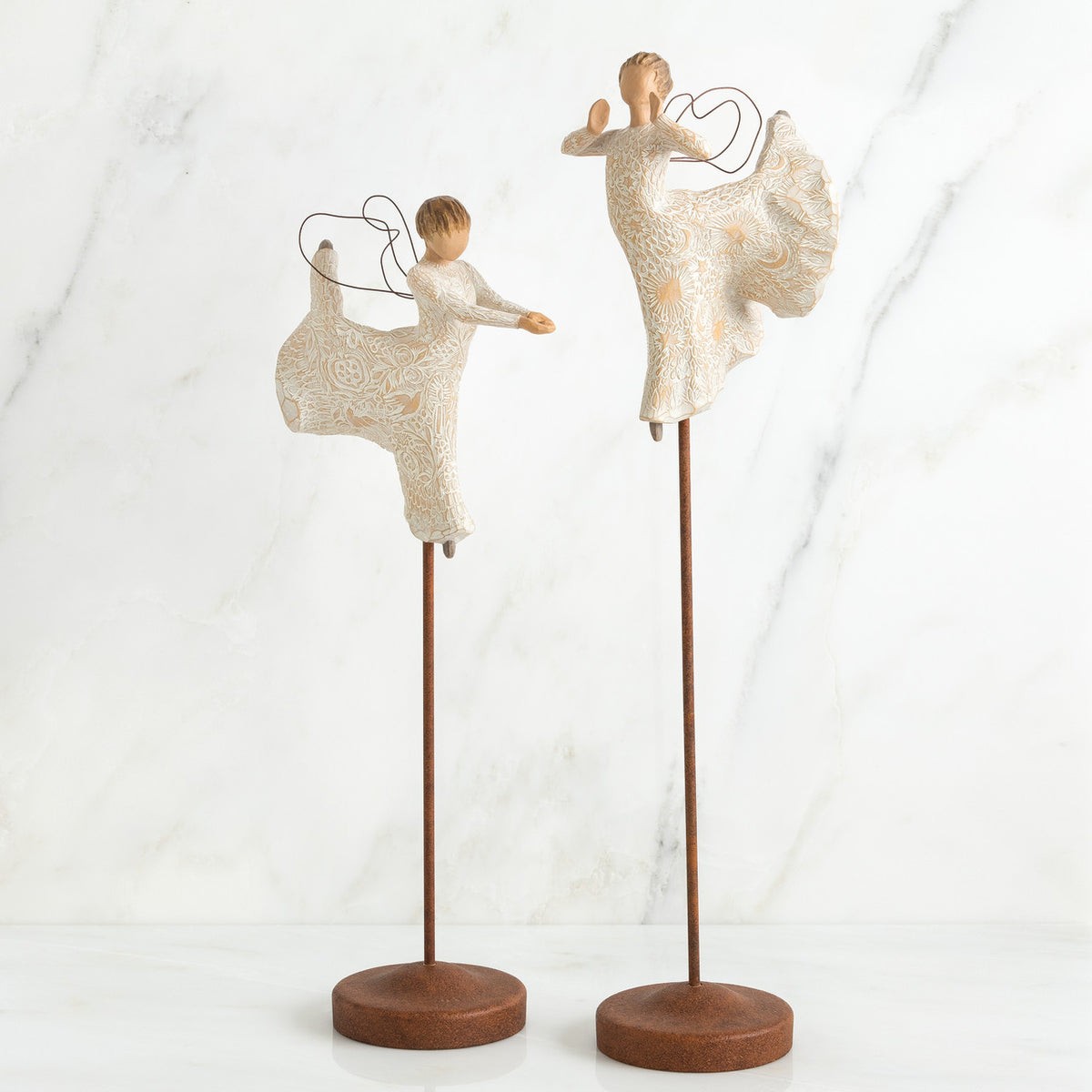 Two angel figurines dancing on top of wooden stands