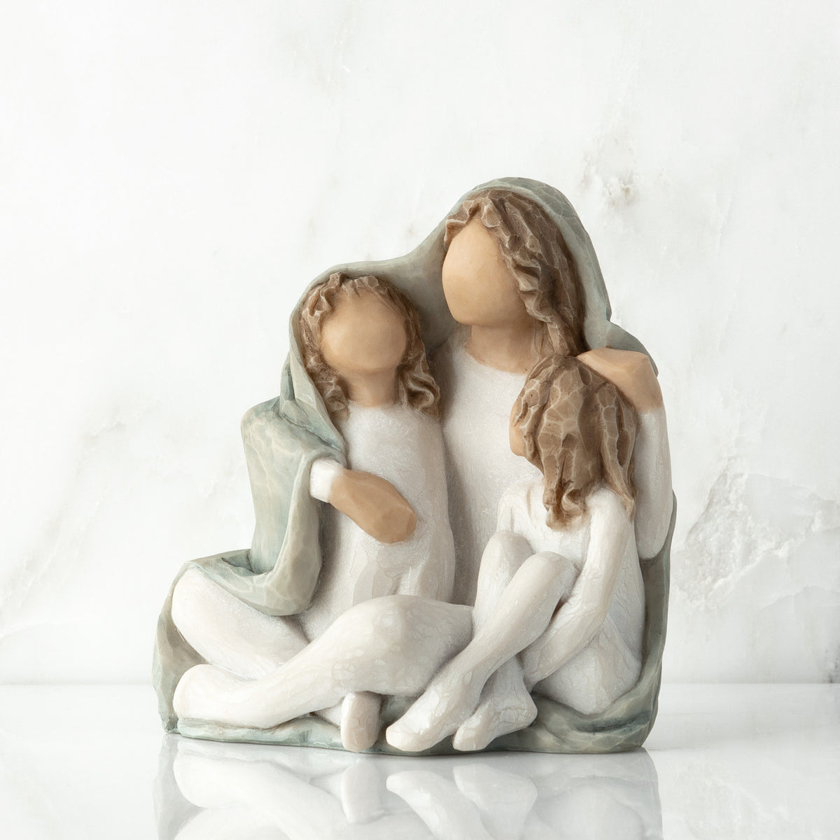 Left view: seated figure with arms around two younger figures, all wrapped in a blue-gray blanket