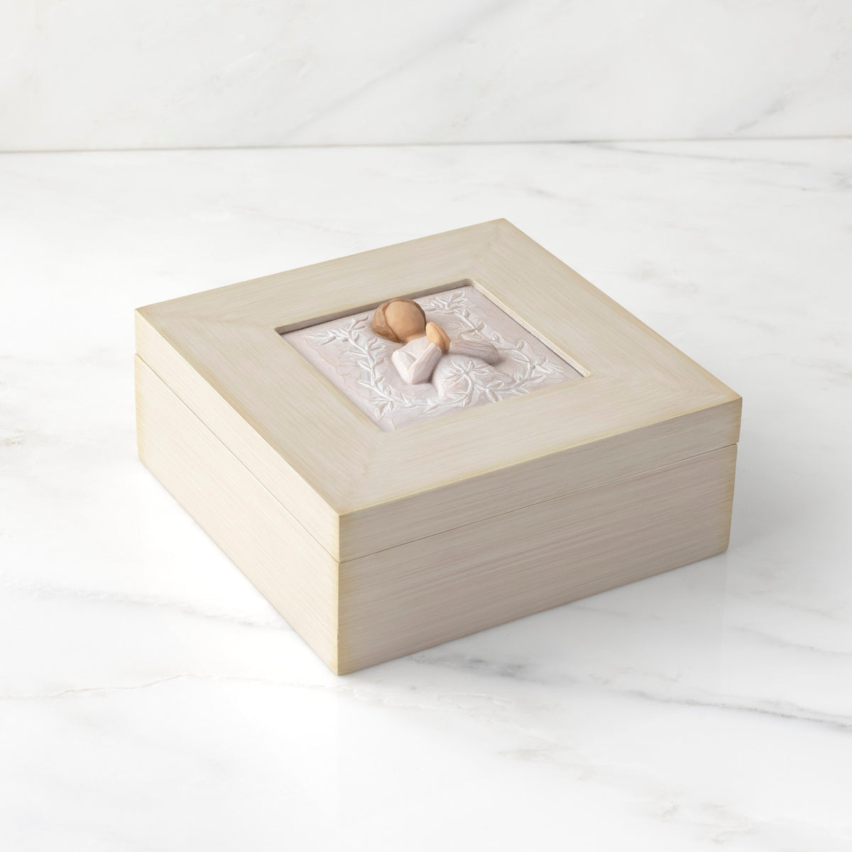 Top down view: Cream square wood box with hinged lid, carving on lid of female in cream dress with hands in prayer position, surrounded by leaves and vines
