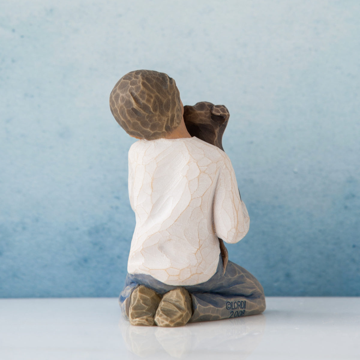 Back view of boy figurine in white shirt and jeans sitting holding puppy