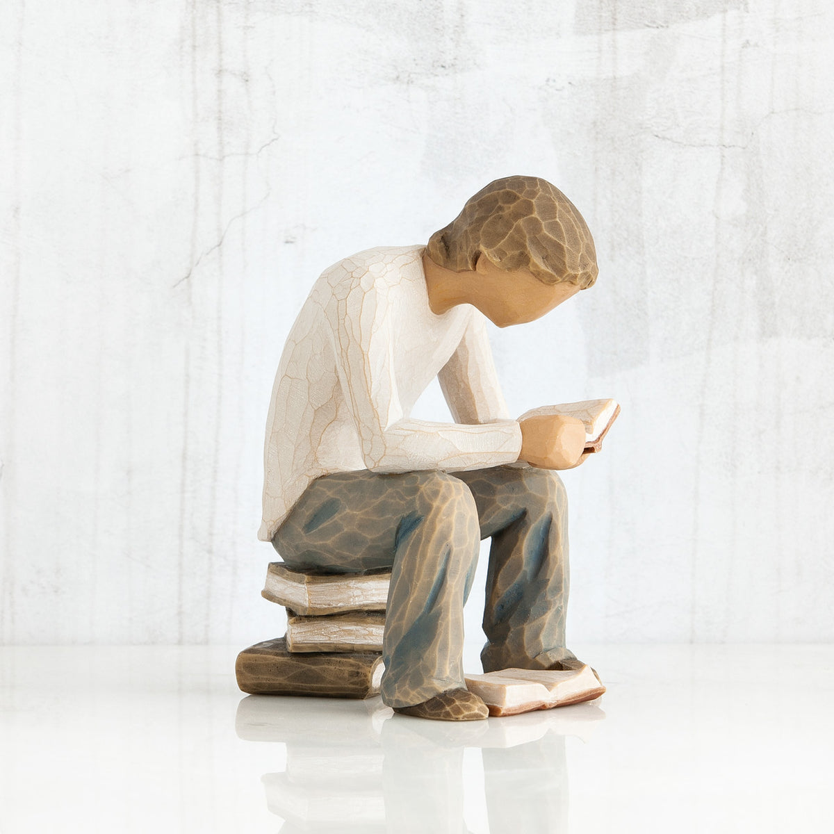 Side view of brunette boy in white shirt, blue jeans, sitting on book stack
