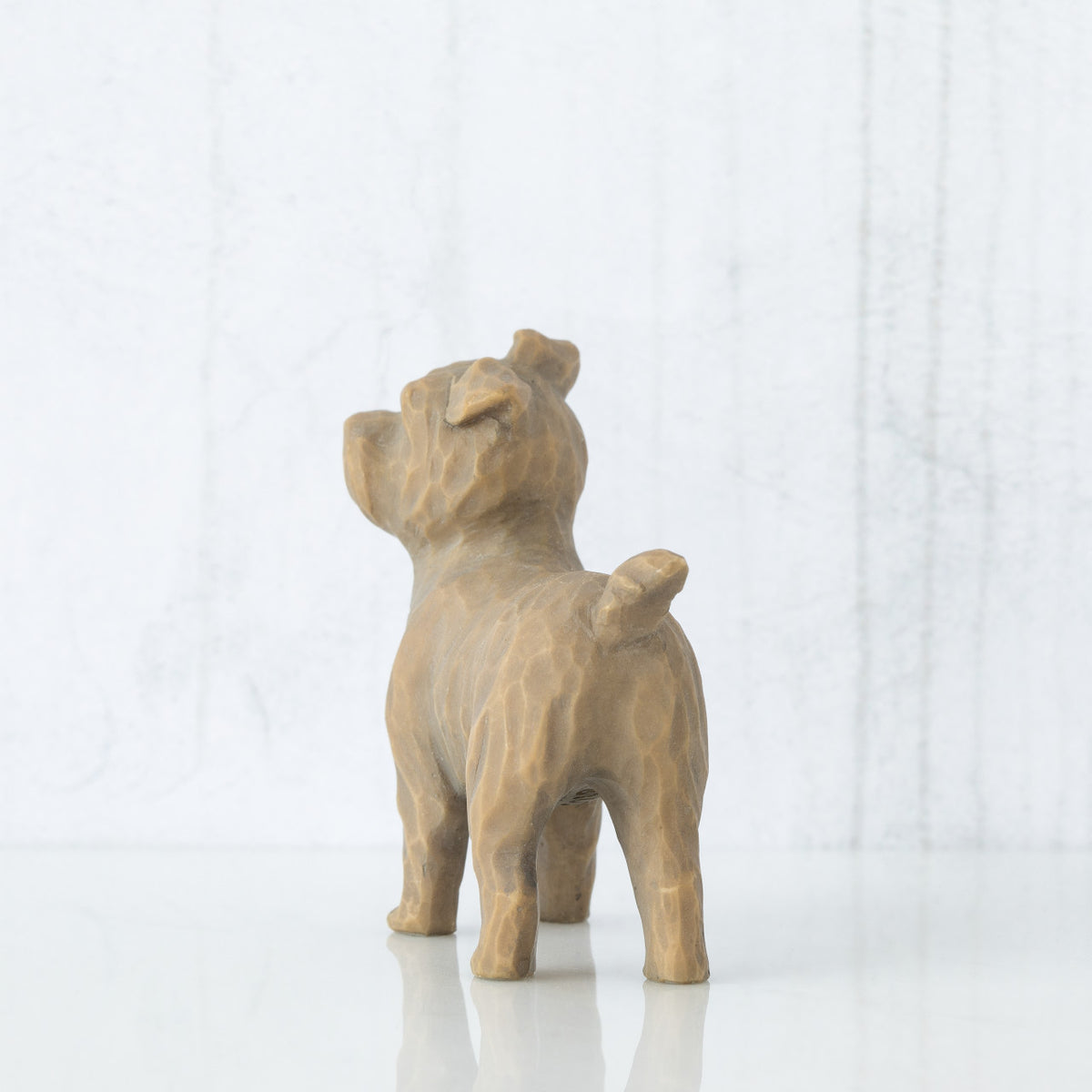 Figure of small brown dog standing on four legs, facing back