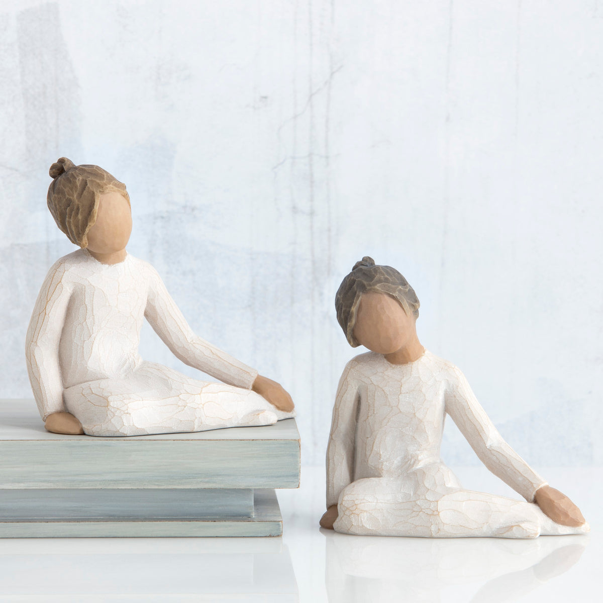 Two young girl figurines sitting in white dresses facing forward