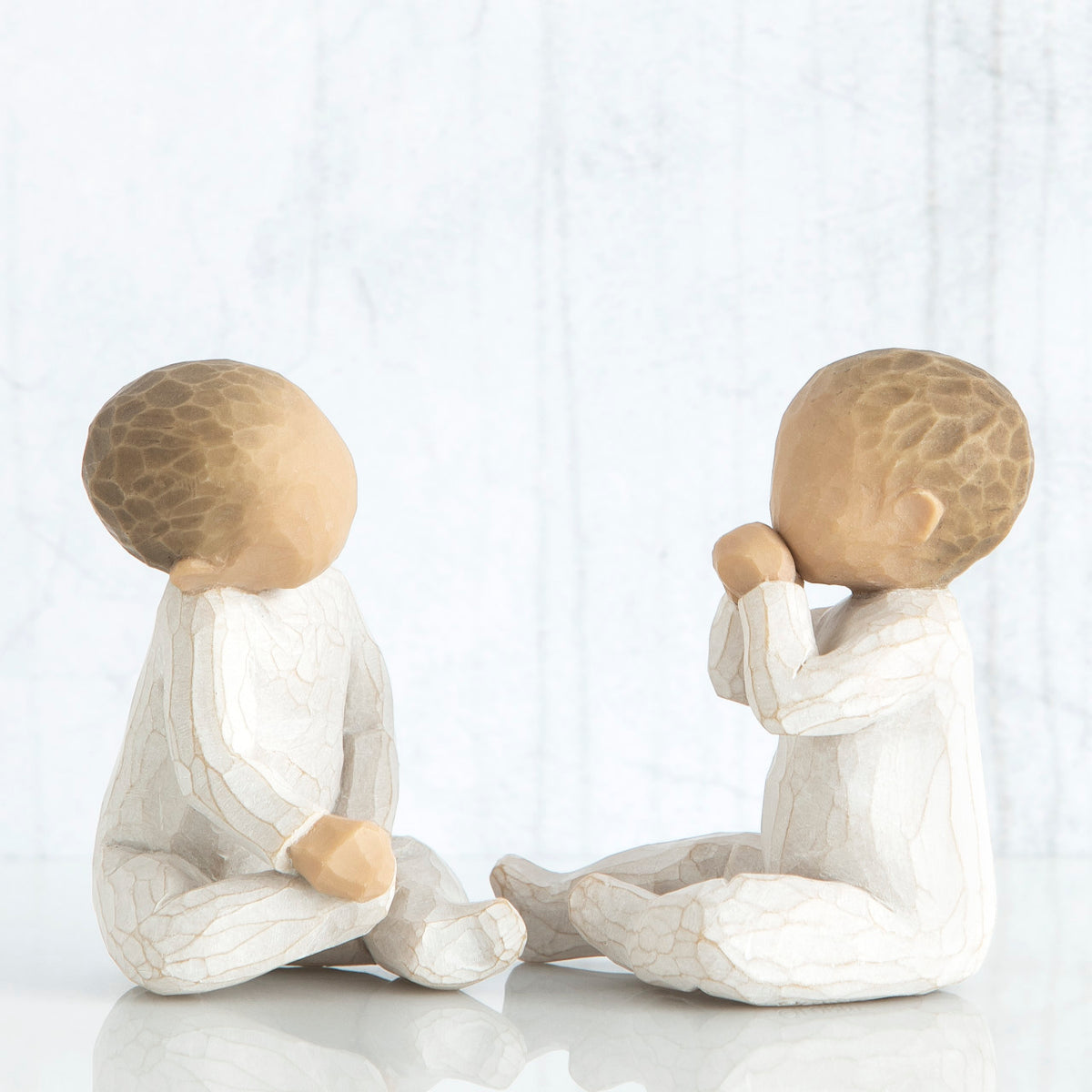 Side view of two young brunette baby figurines sitting in white
