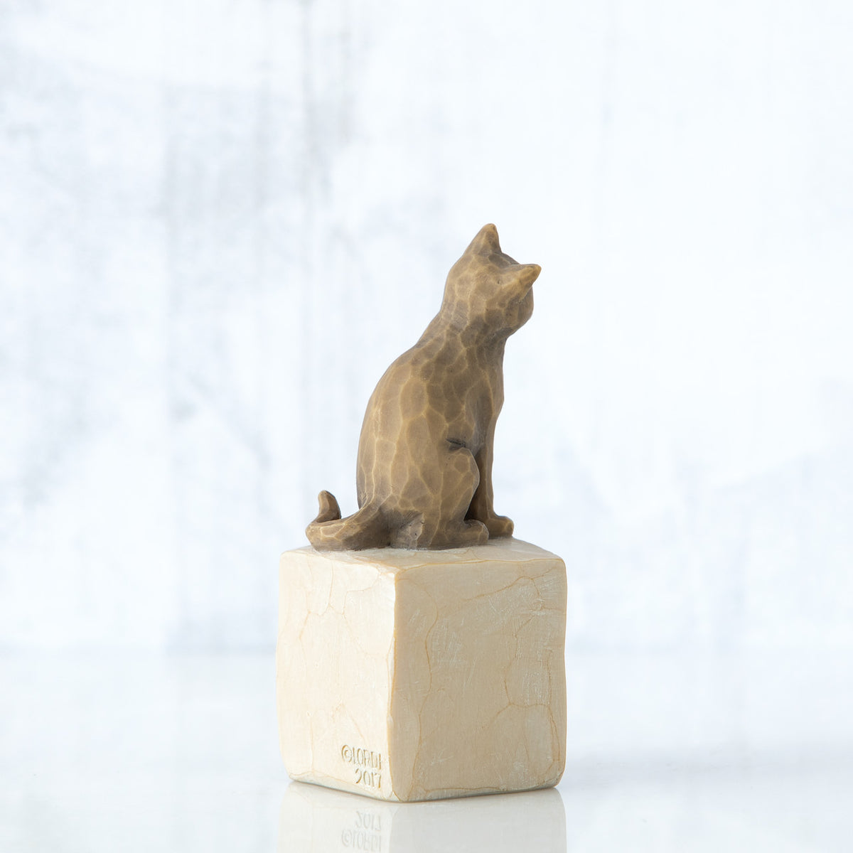 Golden cat figurine facing away sitting on cream square rock