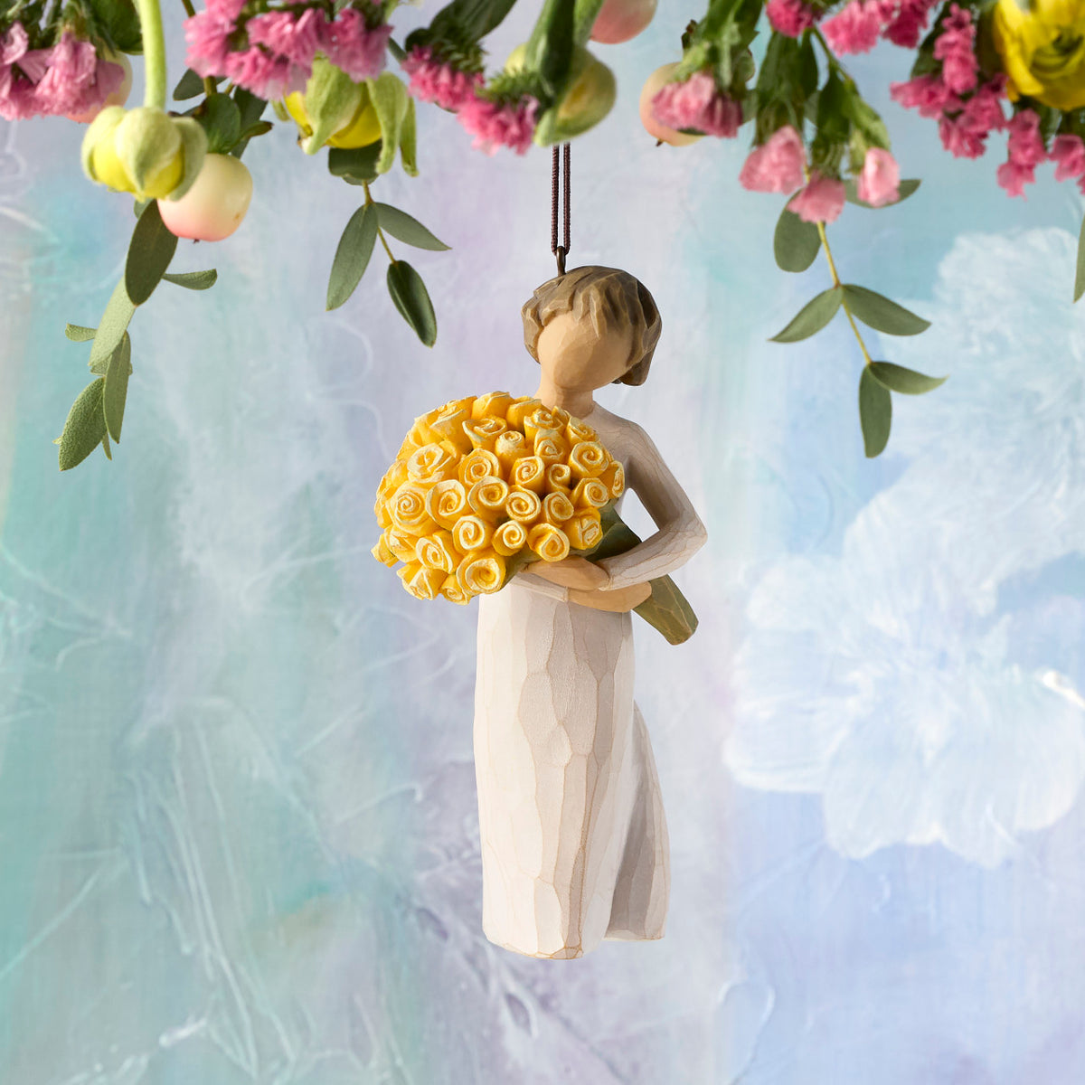 Willow Tree Good Cheer! Ornament, 4.5”h hand-painted resin figure in cream dress, holding bouquet of yellow roses, brown elastic cord, hanging in front of sky blue painting
