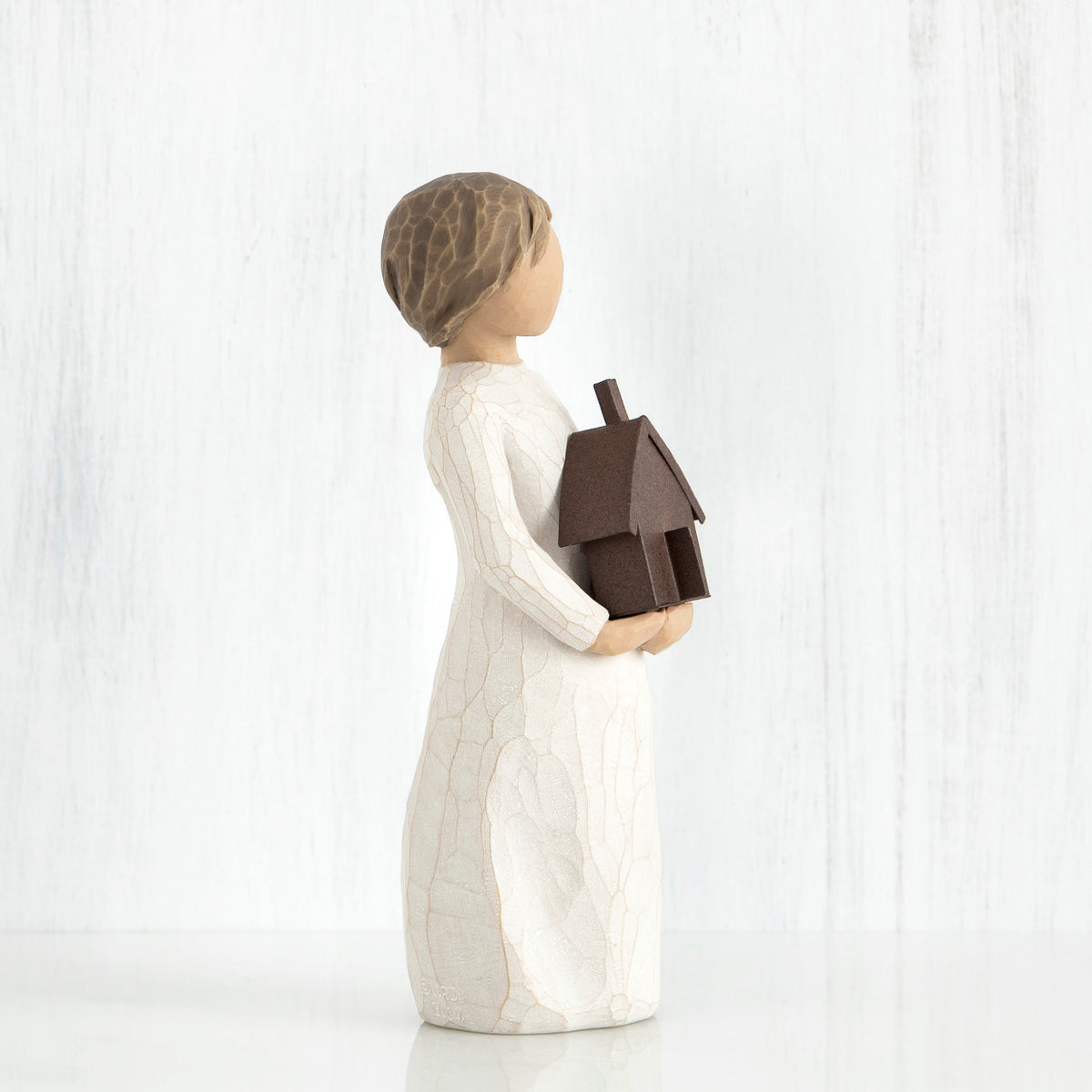 Small brown haired girl figurine in white dress holding brown house figurine