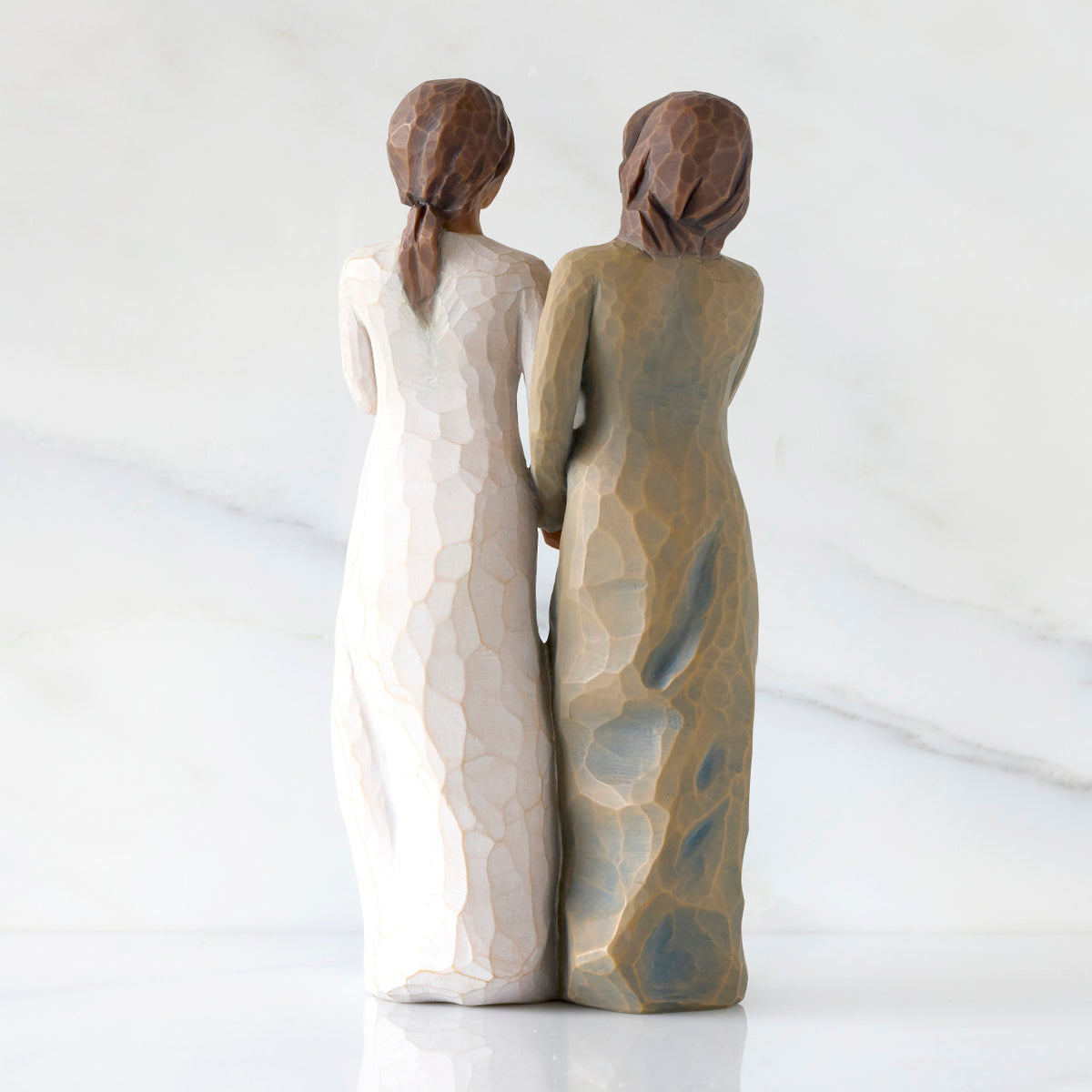 Back view: Figure of two women with darker skin tones in different colored dresses, standing arm in arm