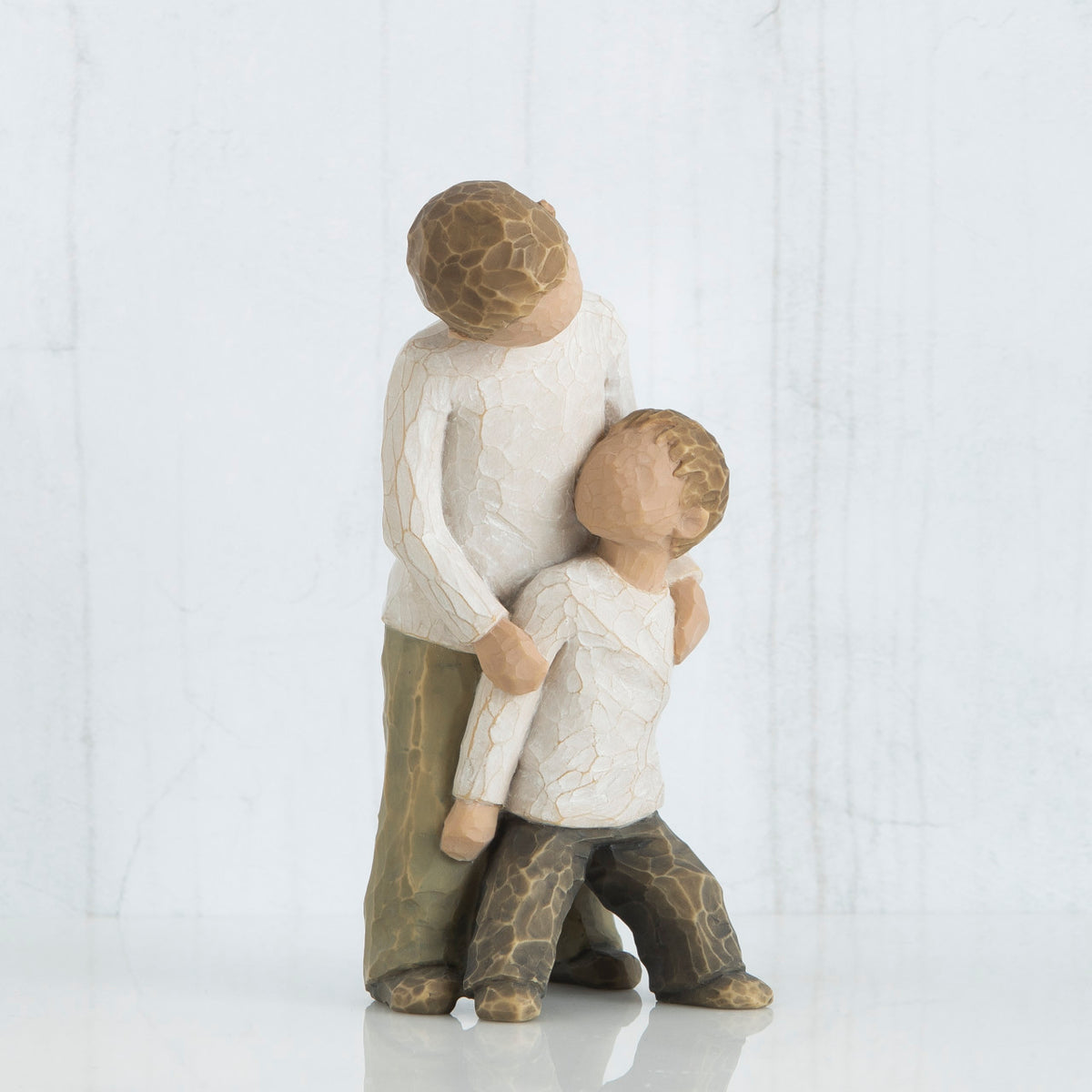 Two young boy figurines in white shirts and brown pants holding hands