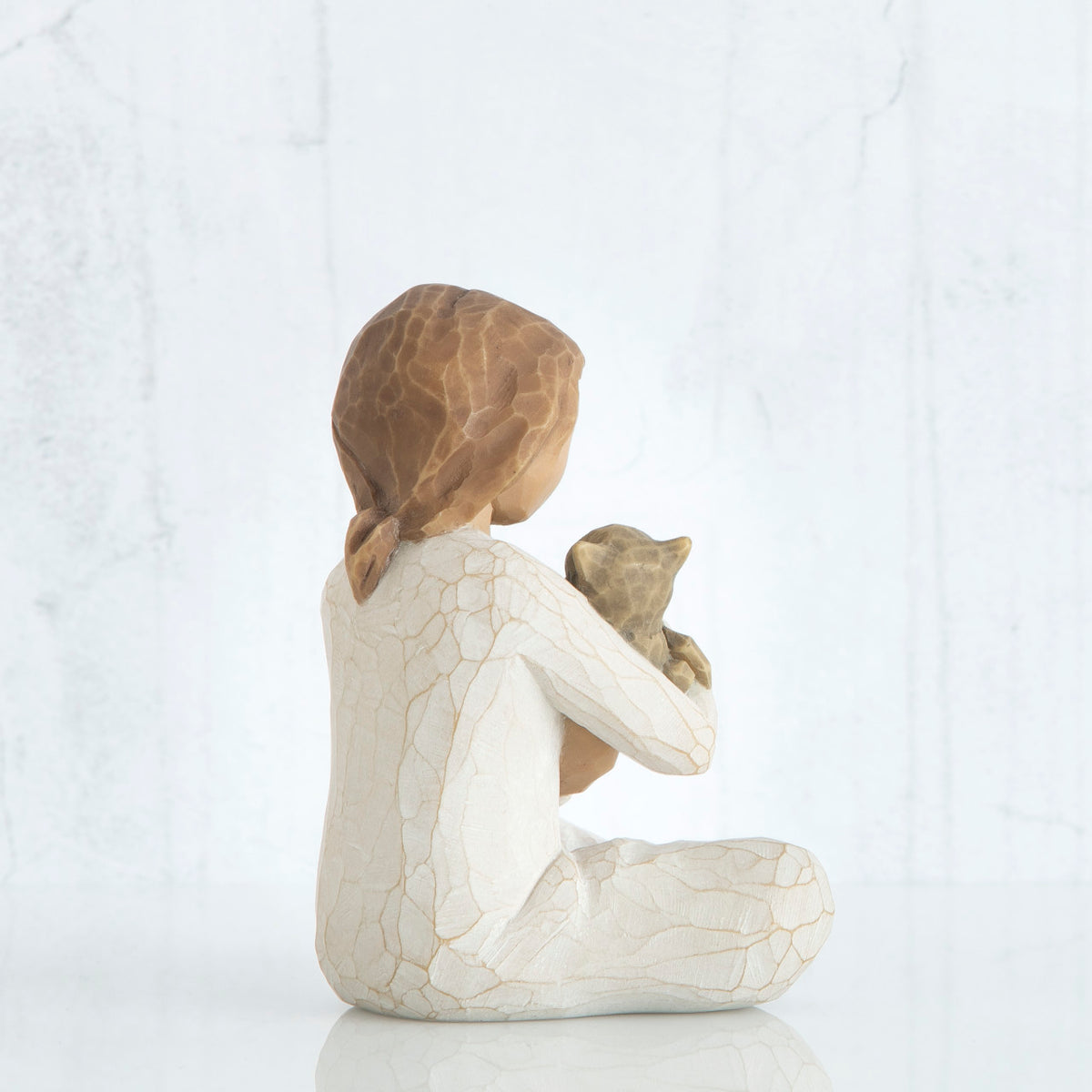 Back view of young girl with light brown hair sitting cross legged and holding a brown cat in her arms, both cat and girl gaze at each other