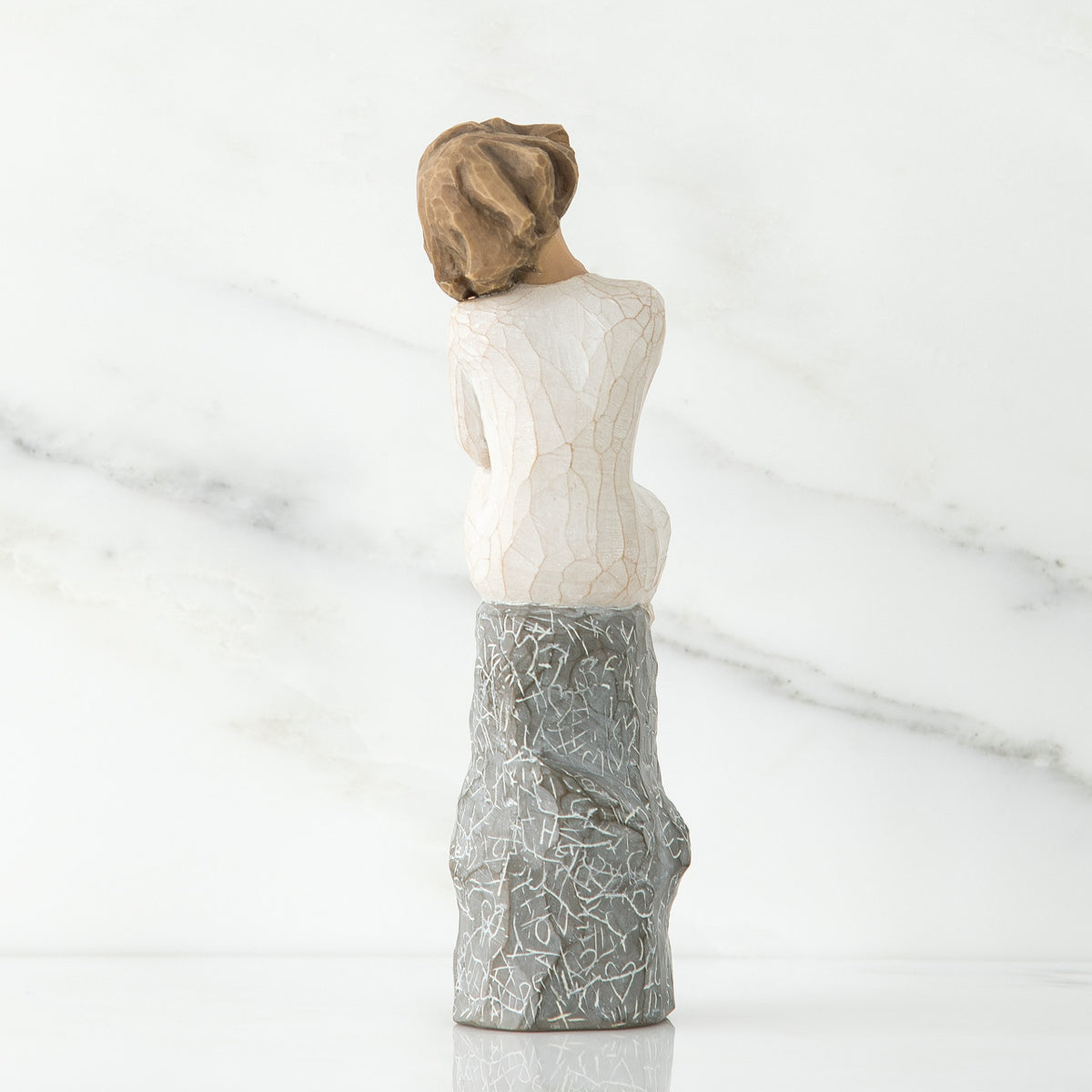 Brunette girl figurine in white facing away from camera sitting on grey rock