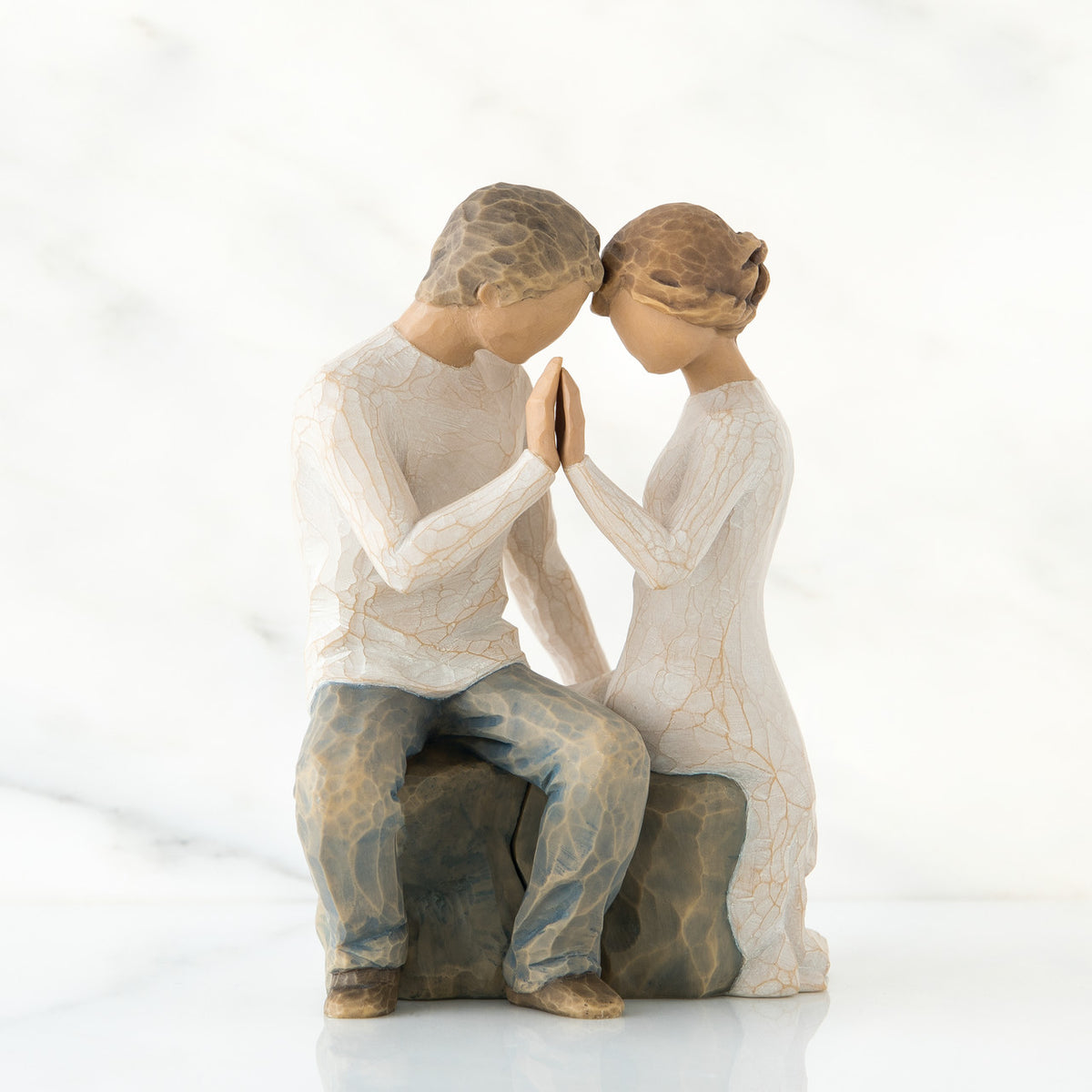 Man and woman figurine sitting on rock dressed in white pressing their hands up against each others