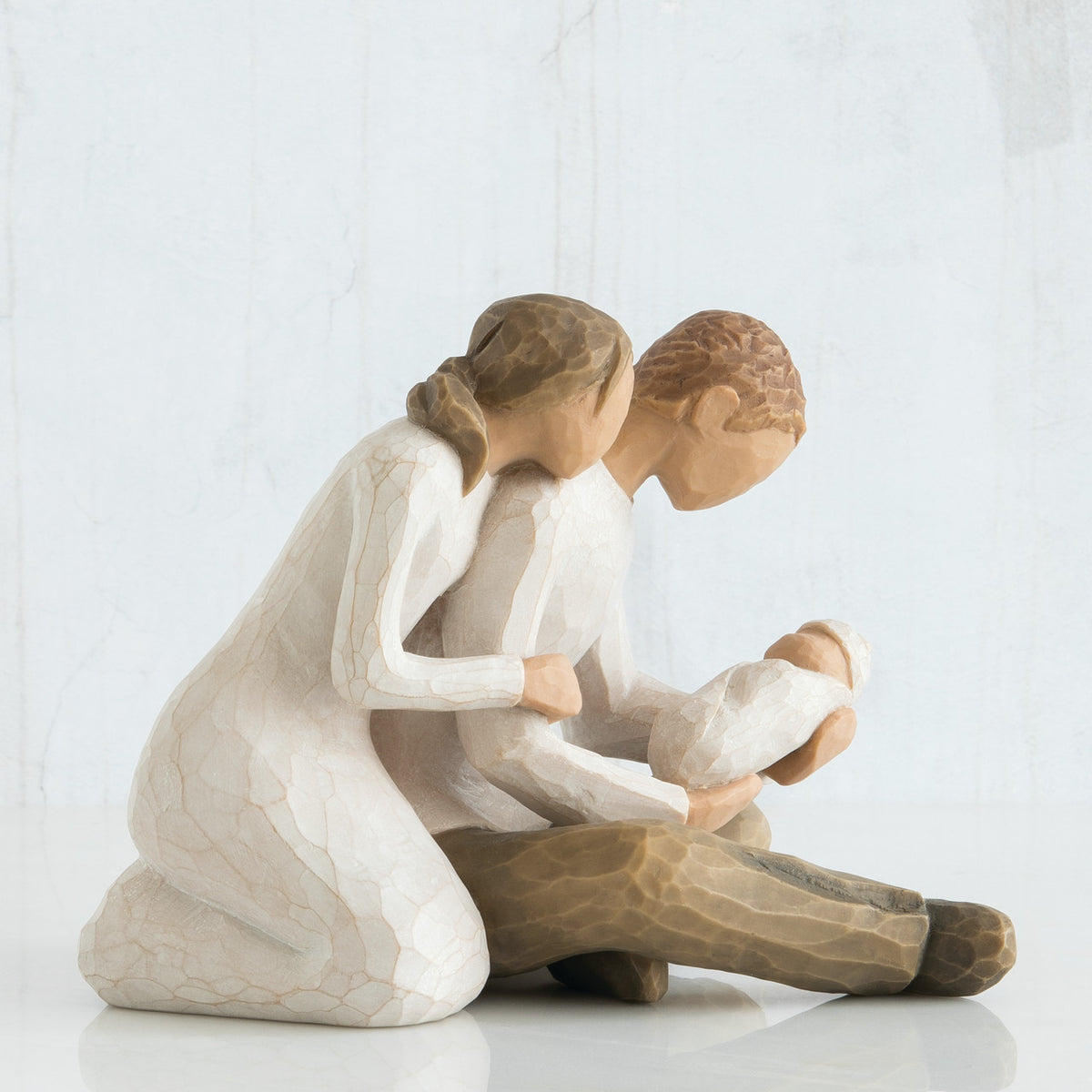 Man and woman figurines sitting down holding baby wrapped in white