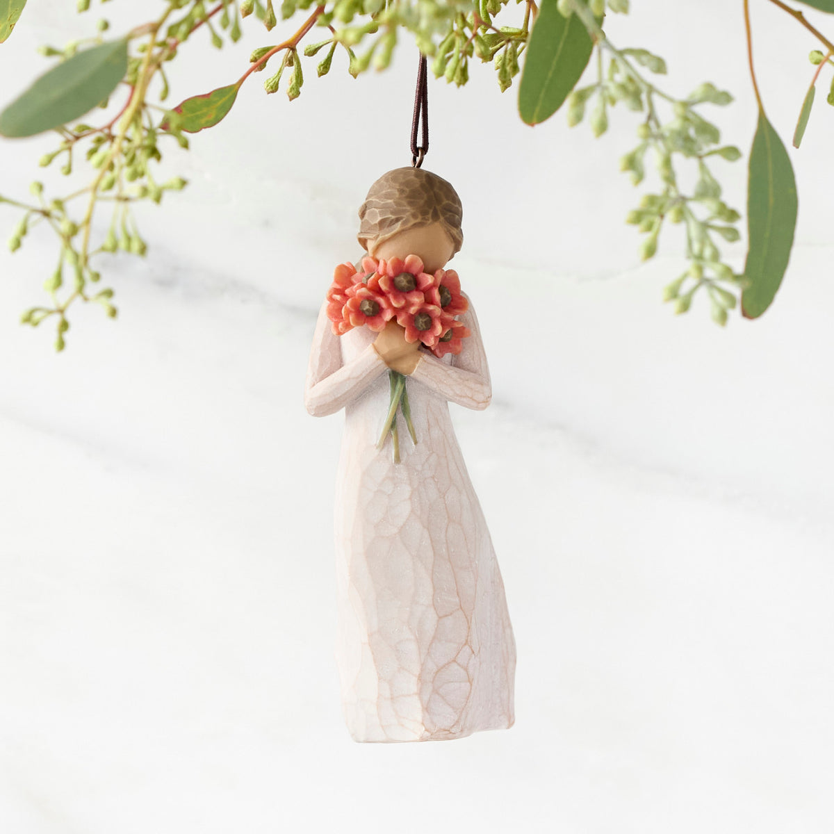 Figure in cream dress holding large bouquet of red-orange poppies up to face, ornament hook attached to head