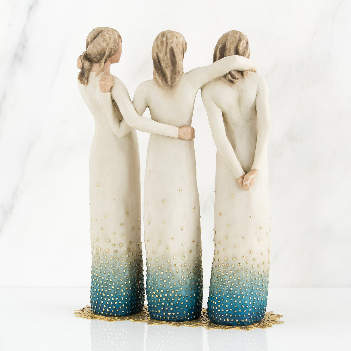 Set of three woman figurines wearing white/blue dresses facing the back with arms around each other
