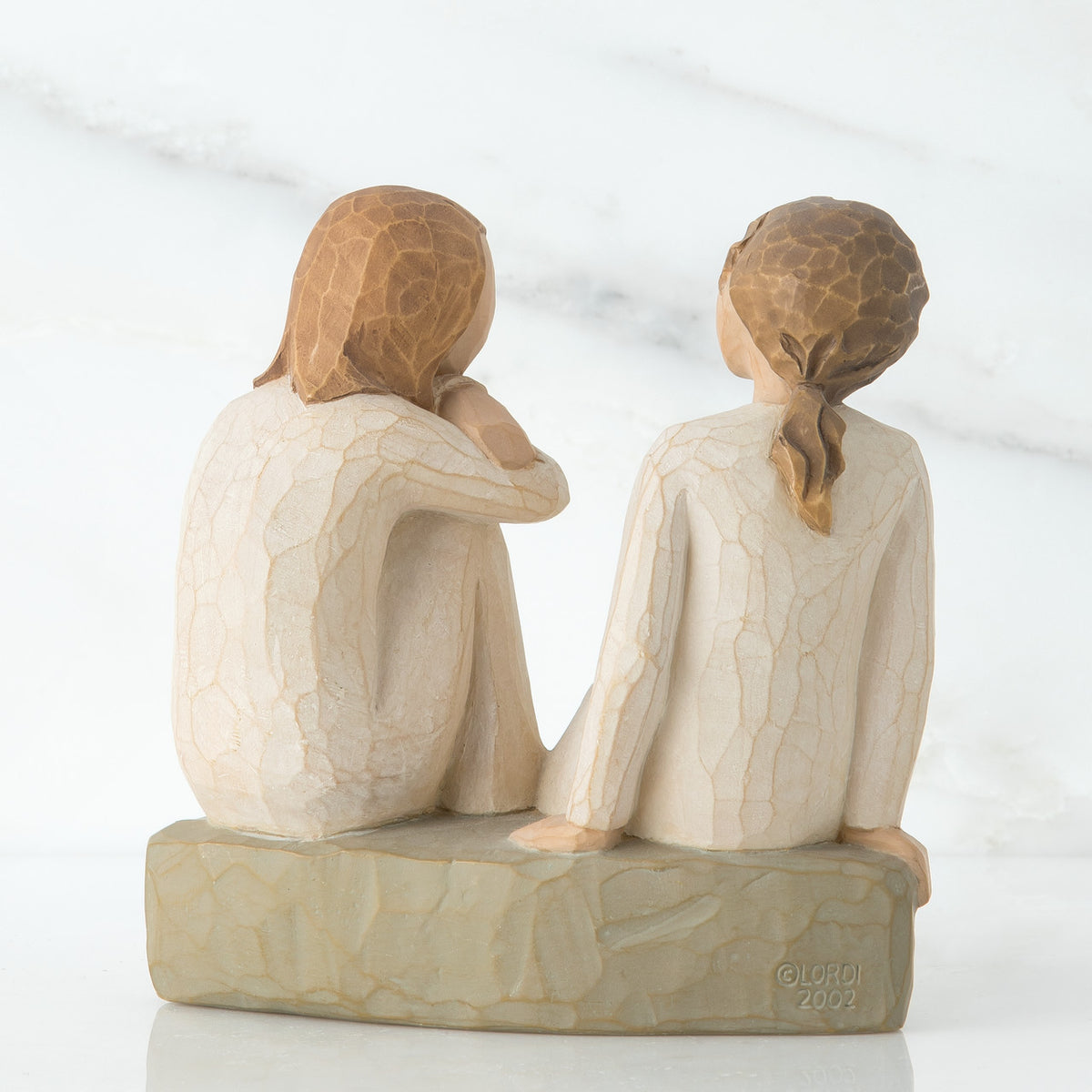 Back view of two brunette girl figurines in white sitting on a grey rock