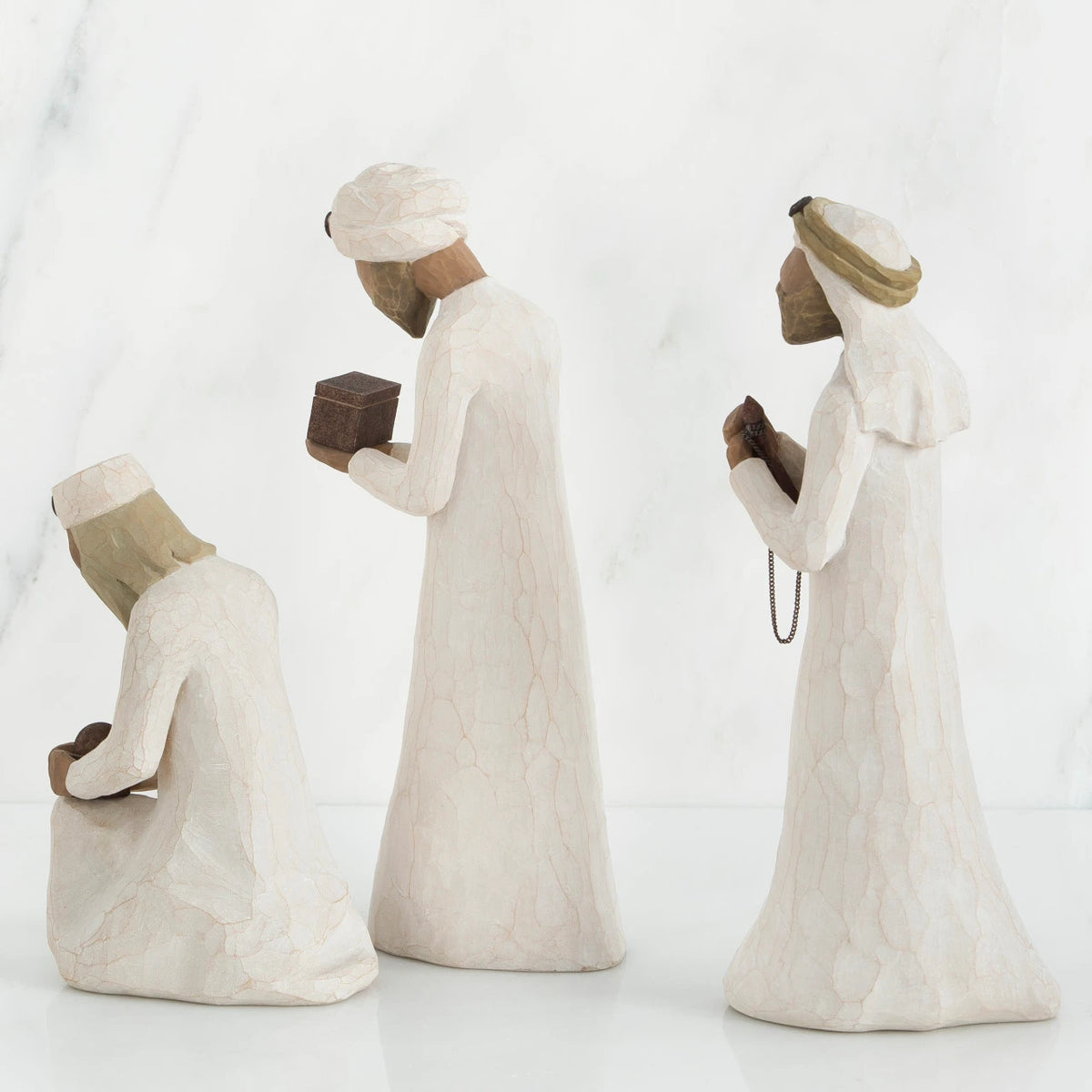 Three wiseman figurines in white dresses facing the side holding brown boxes