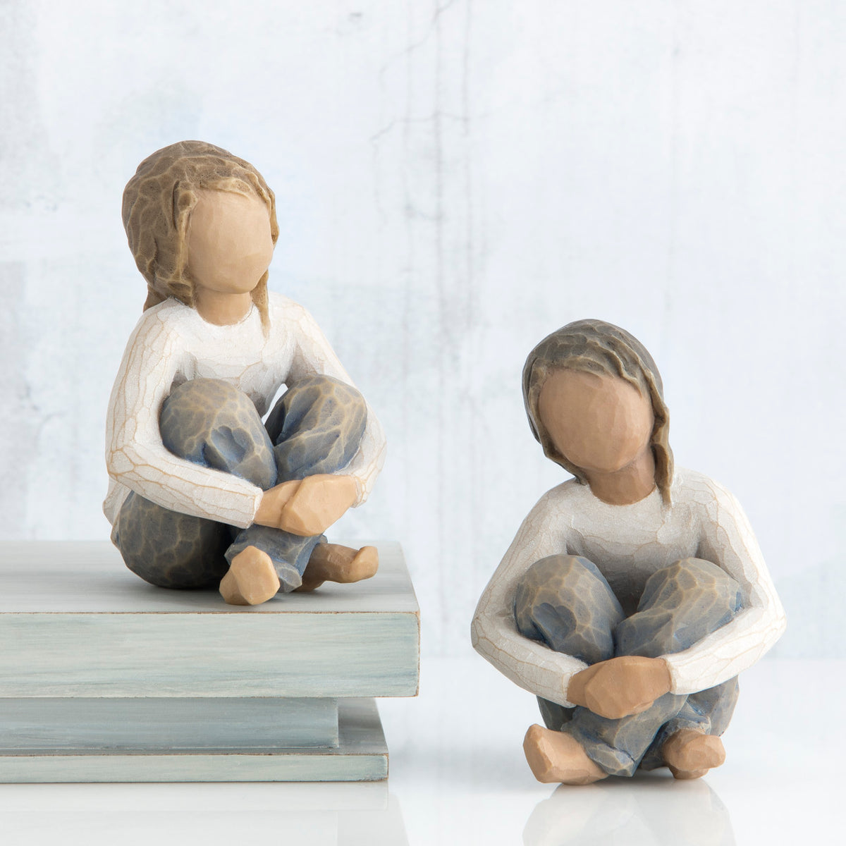 Two young brunette girl figurines sitting down in white shirts and blue jeans