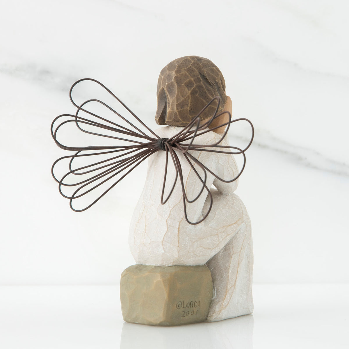 Back view of angle with brown hair sitting on a stone with her hands cupping her cheeks