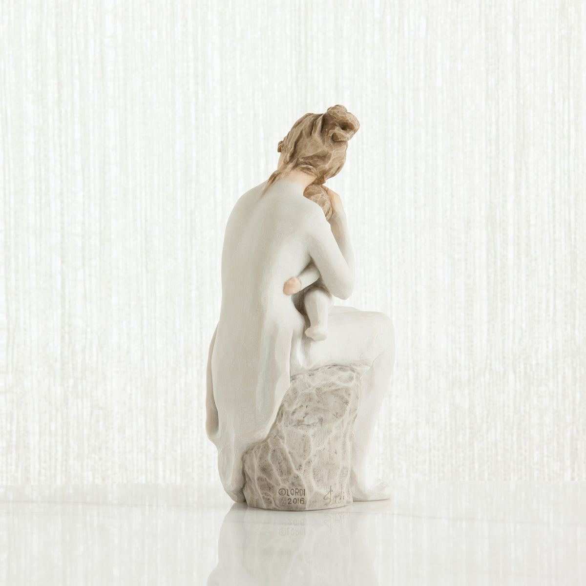 Woman figurine dressed in white sitting on rock holding baby - back view