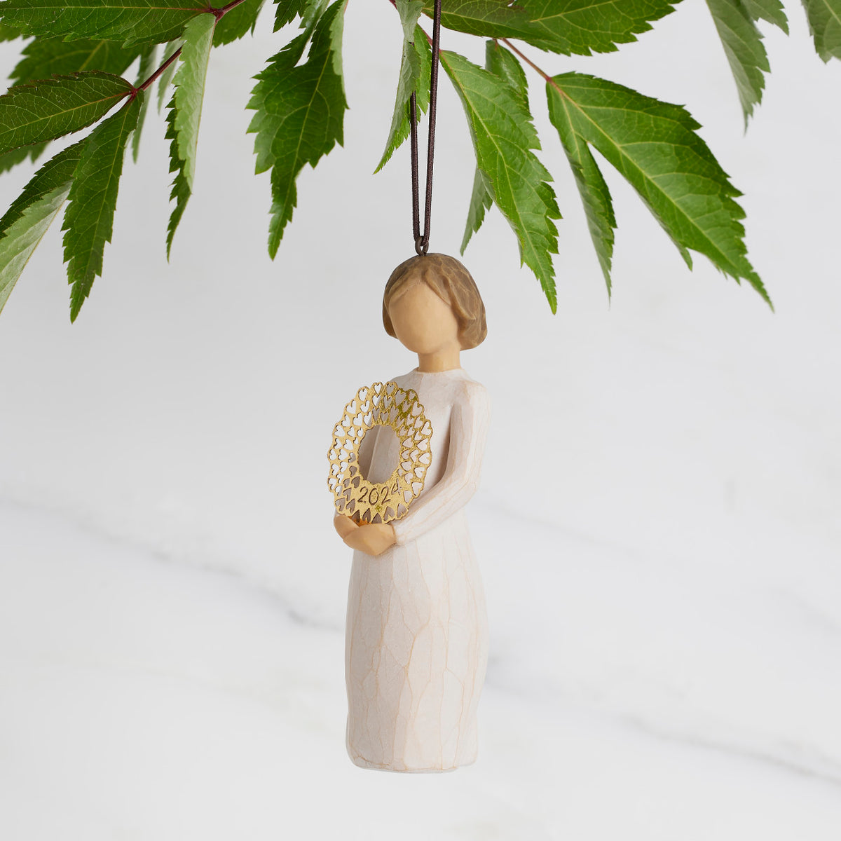 Facing left: Dated Ornament of figure holding pierced gold-leaf wreath of hearts. 2024 written on wreath; loop and hook in head
