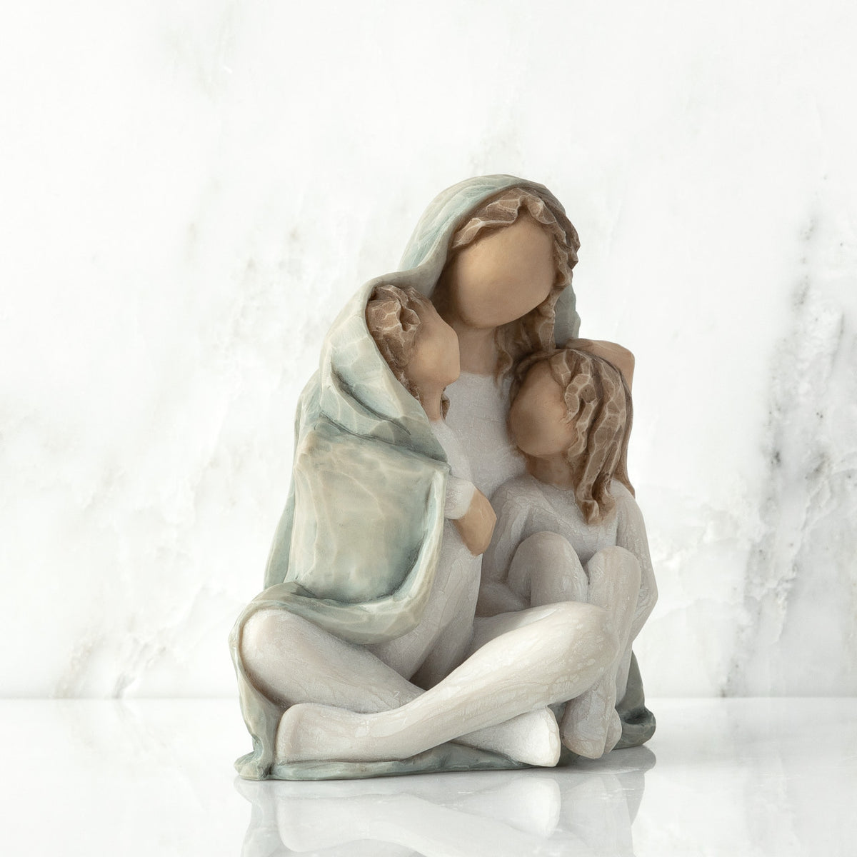 Right view: seated figure with arms around two younger figures, all wrapped in a blue-gray blanket