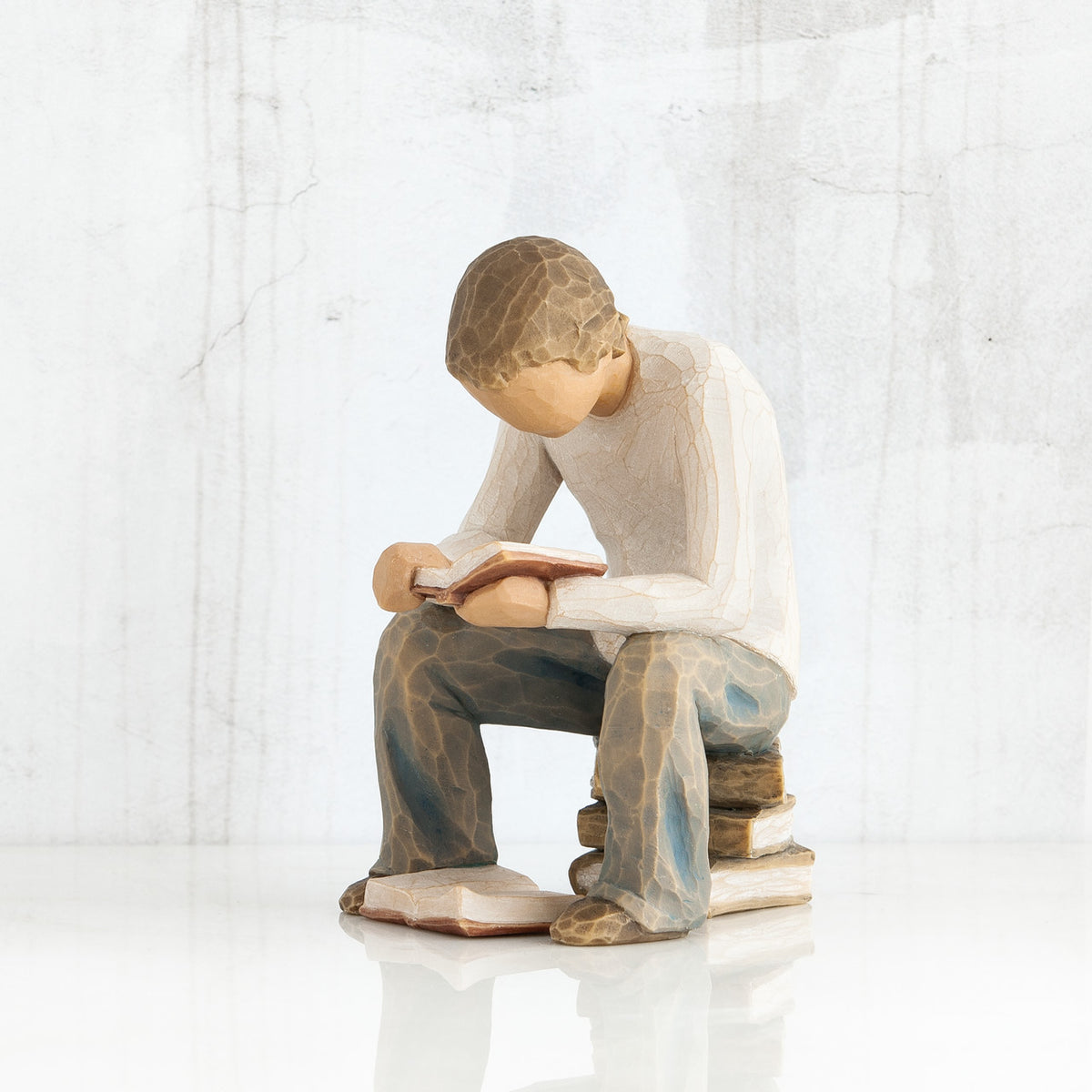Young faceless boy figurine sitting on books with book opened in his hands - another book on the floor of his feet
