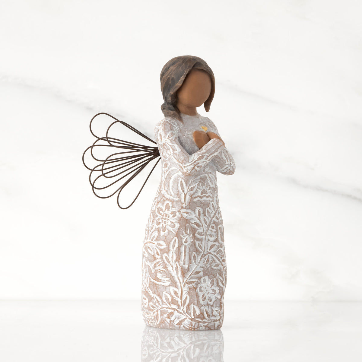 Facing right: angel with wire wings, darker skin, arms crossed over gold heart, dress carved with symbols of remembrance