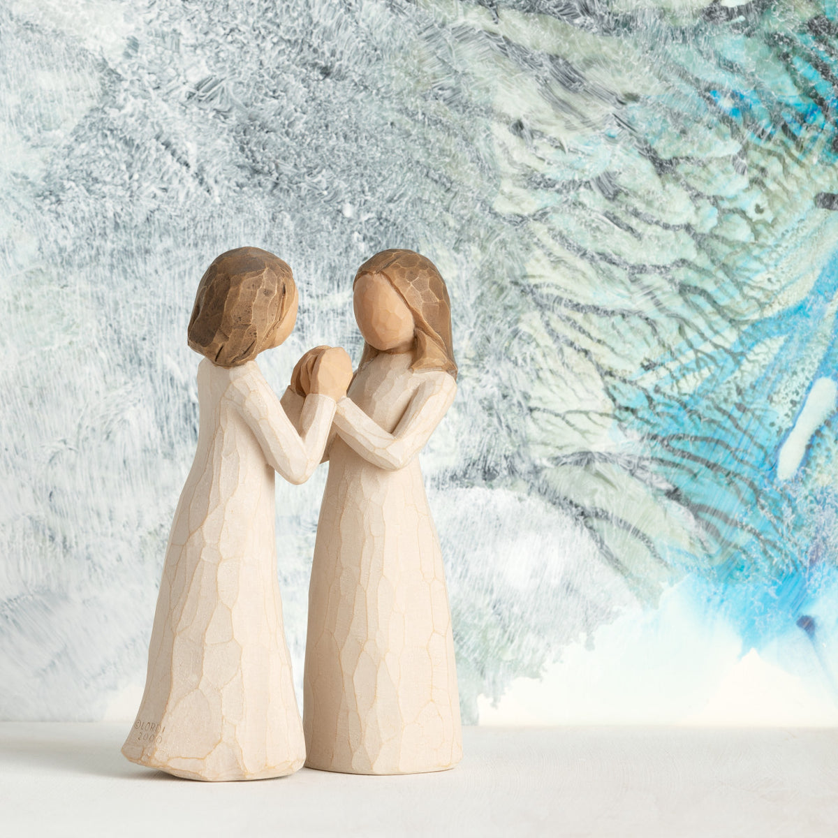 Willow Tree Sisters by Heart, two separate 4.5”h hand-painted standing resin figures in cream dresses with hands that fit together, in front of blue and celadon painting