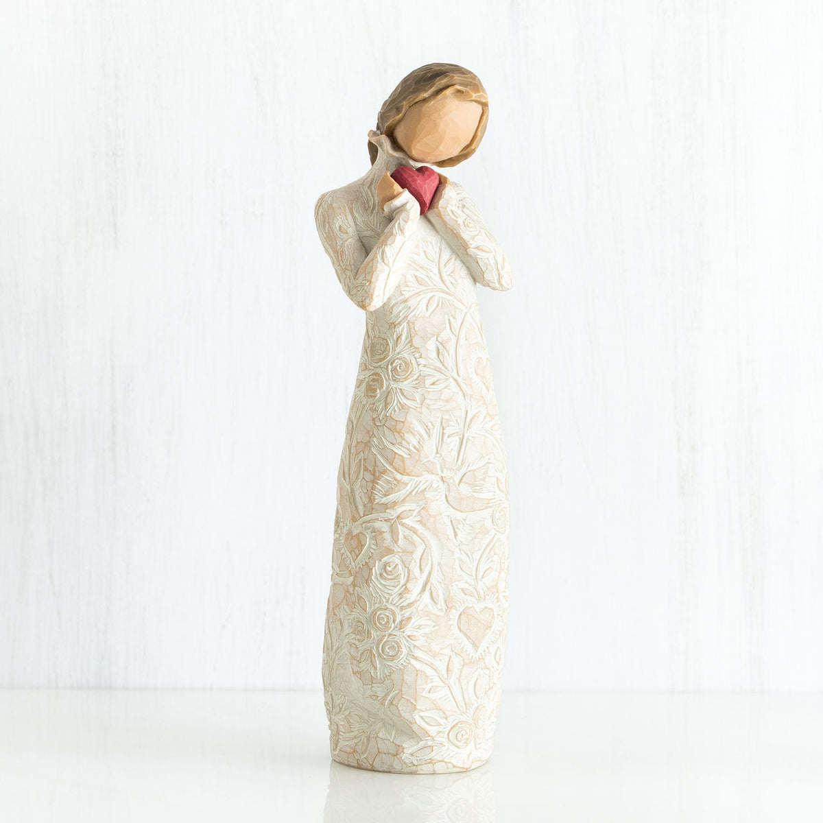 Standing faceless woman figurine in white dress facing forward holding pink heart
