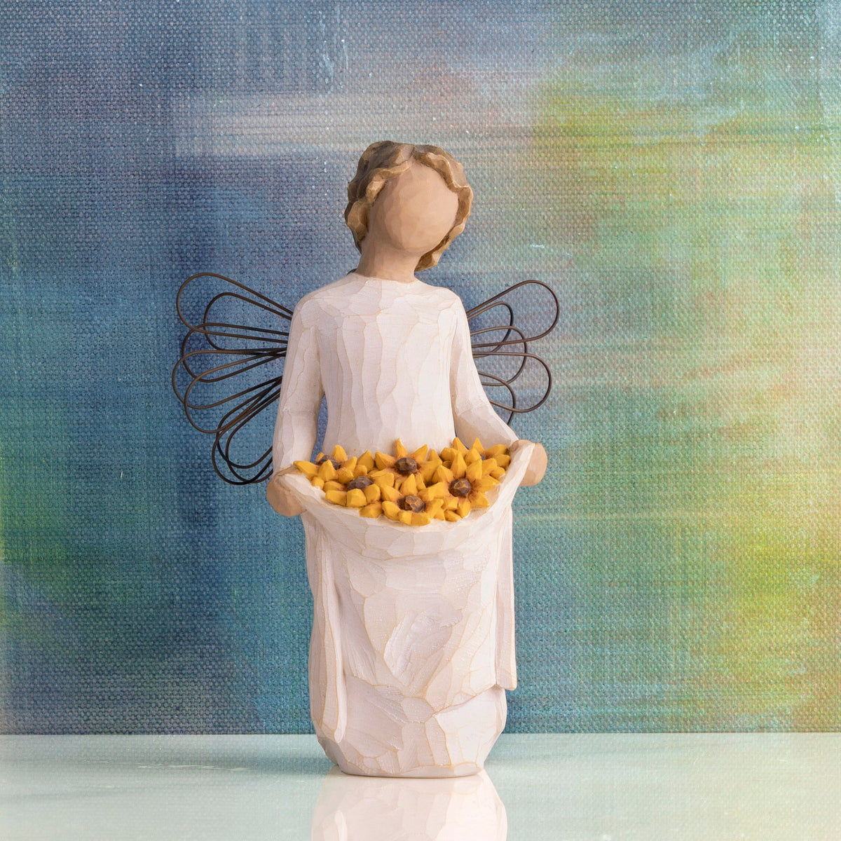 Willow Tree Sunshine, 5.5”h hand-painted standing resin angel with darker skin and hair, cream dress and wire wings, holding up skirt full of Black-Eyed Susans, in front of deep blue painting