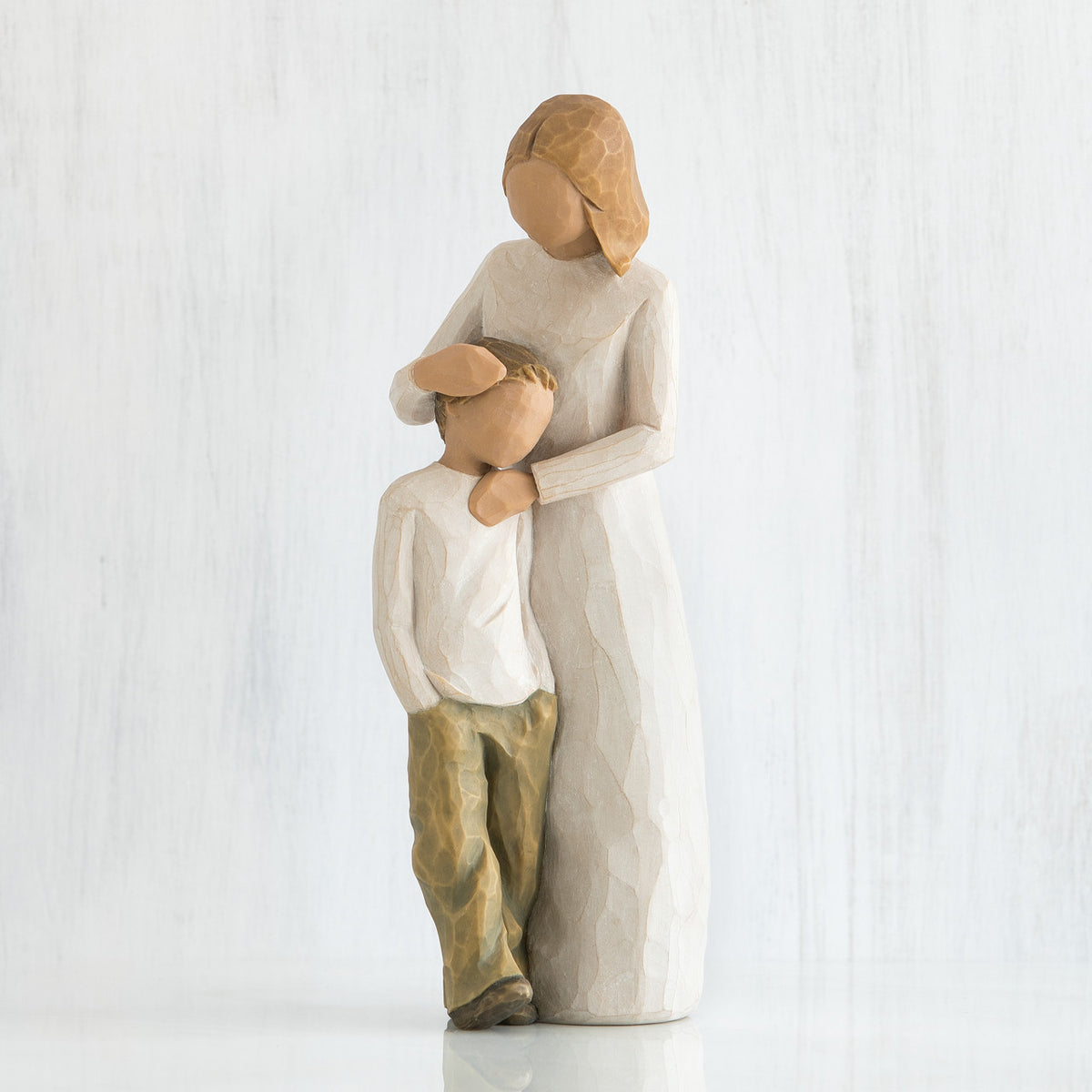 Faceless woman figurine in white dress standing over faceless young boy in white shirt with brown pants