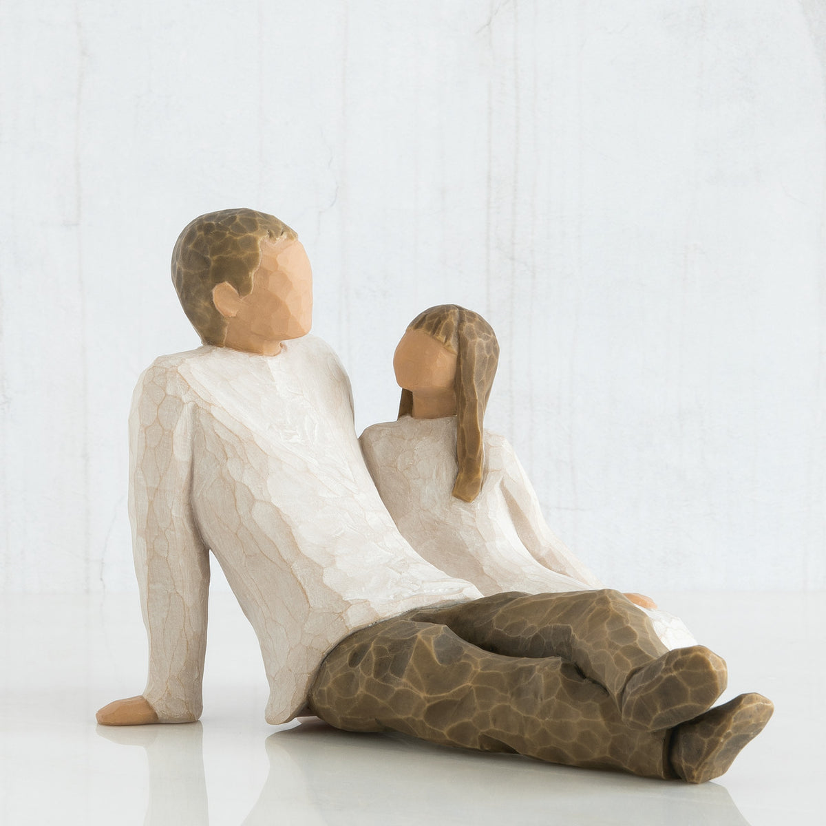 Man figurine and daughter faceless figurines sitting looking at one another - wearing white shirts and brown pants