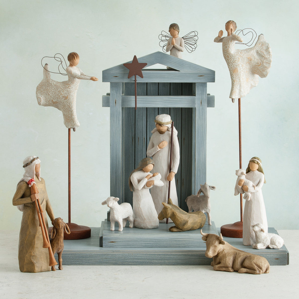 Light grey barn figurine with several wiseman dressed in white, angels, and golden cows laid out