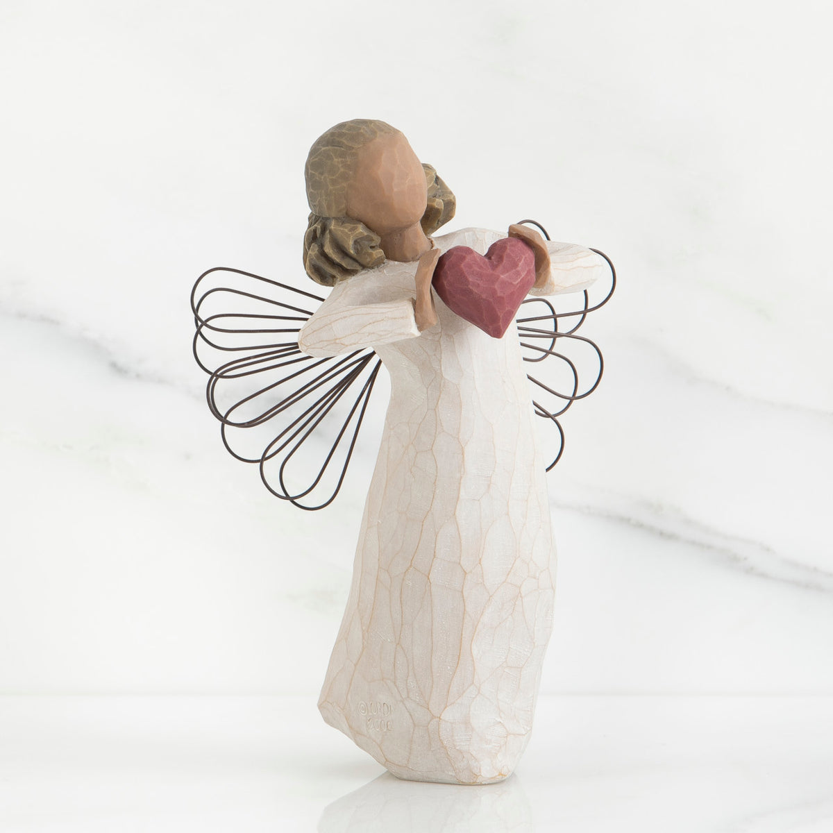 Faceless angel girl figurine wearing white dress and black wire wings holding maroon heart in her hands