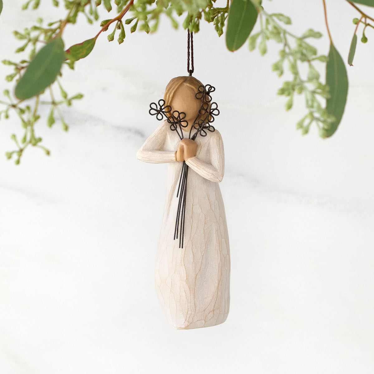 Figure with short light hair in cream dress holding bunch of wire flowers at her face, ornament hook attached to head