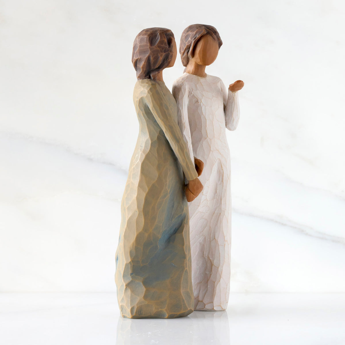 Right-facing view: Figure of two women with darker skin tones in different colored dresses, standing arm in arm