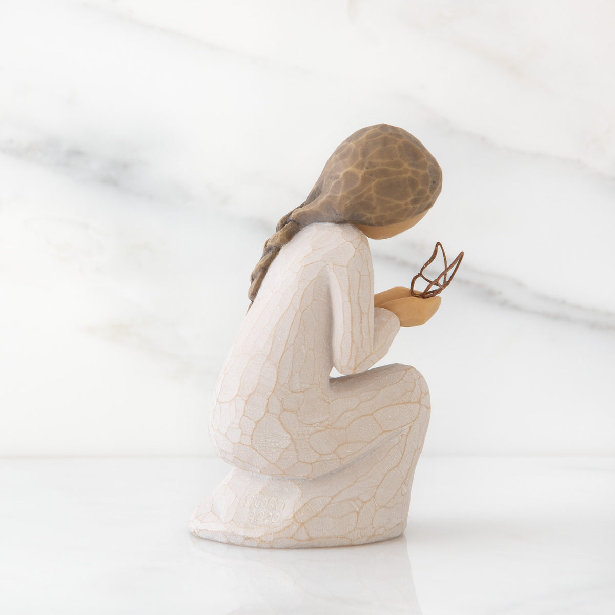 Right side view of kneeling female figure in cream dress, with wire butterfly on extended hands