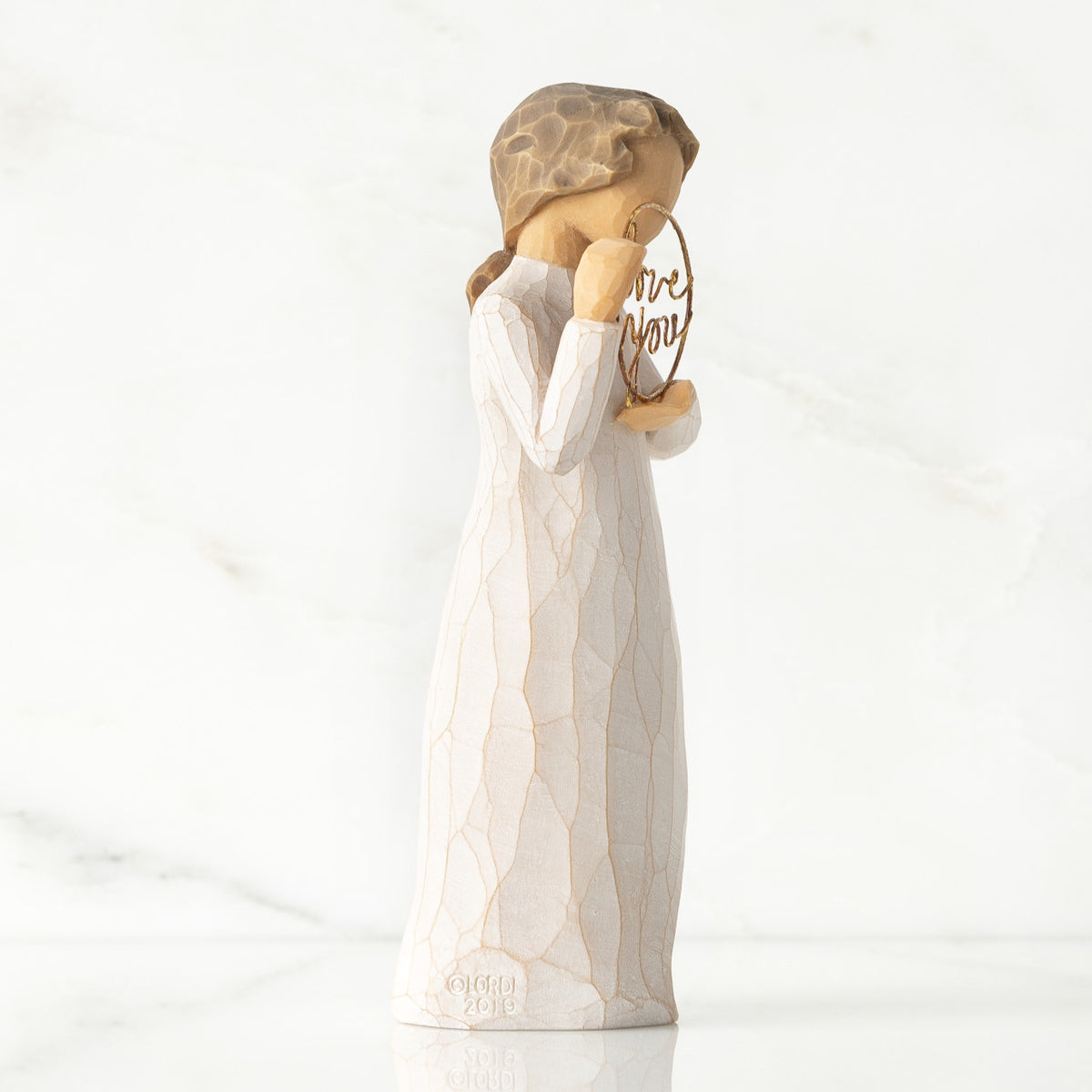 Right-facing view, standing female figure in cream dress, holding gold wire circle in which is written 'love you'